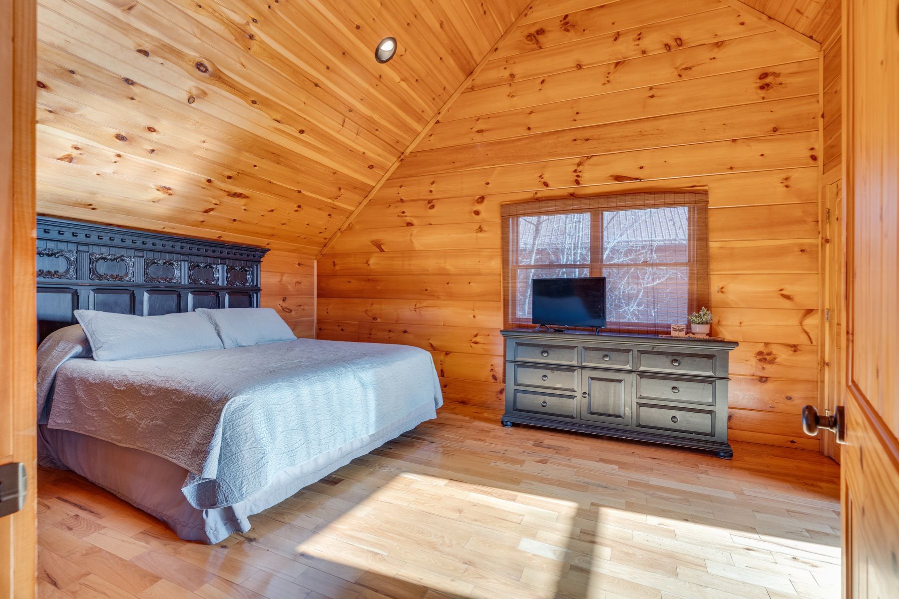 Cozy bedroom with wooden walls and ceiling.  A bed, dresser, and window.