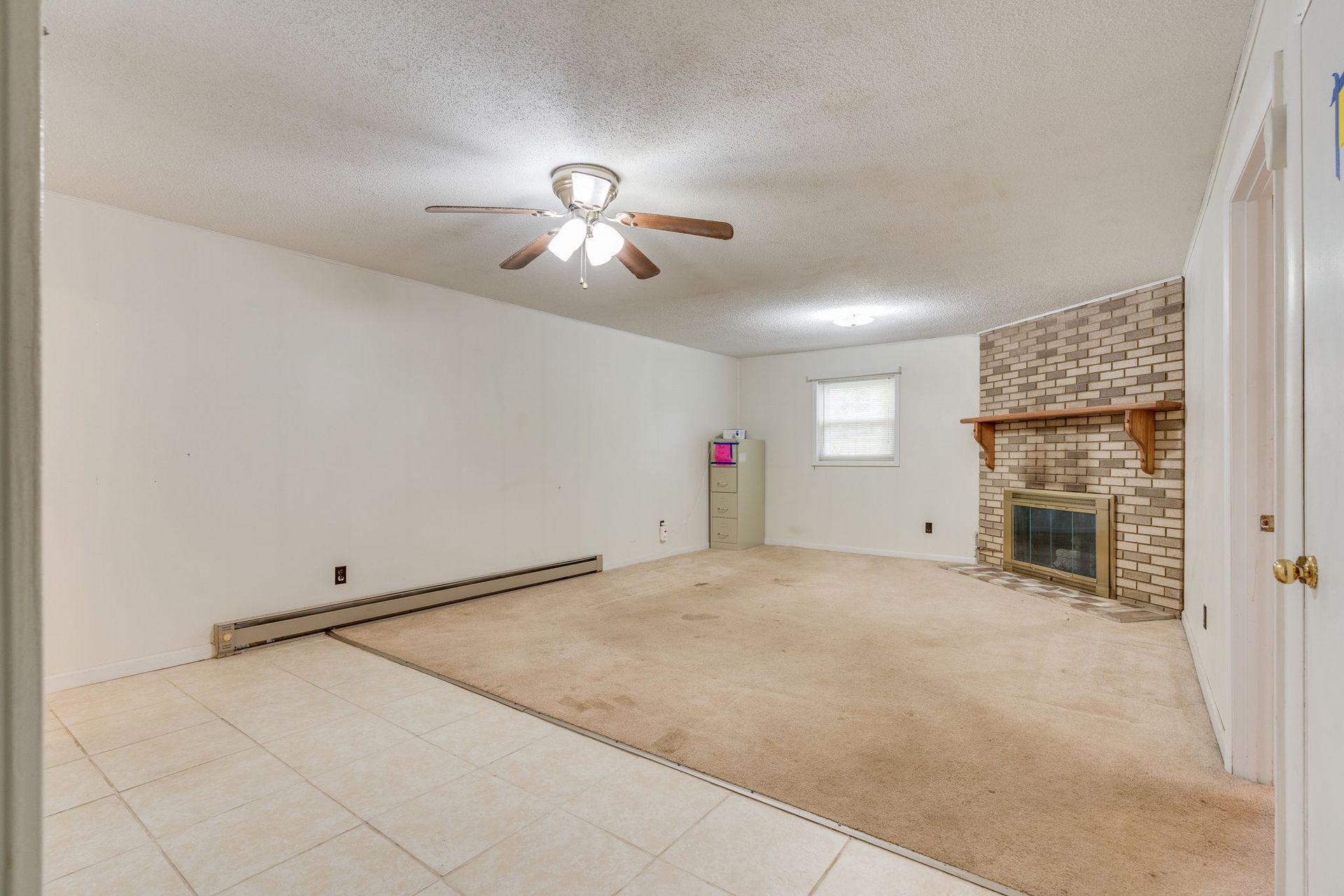 A living room with light tile flooring near the entrance, carpeted main area, a ceiling fan, and a stone fireplace.