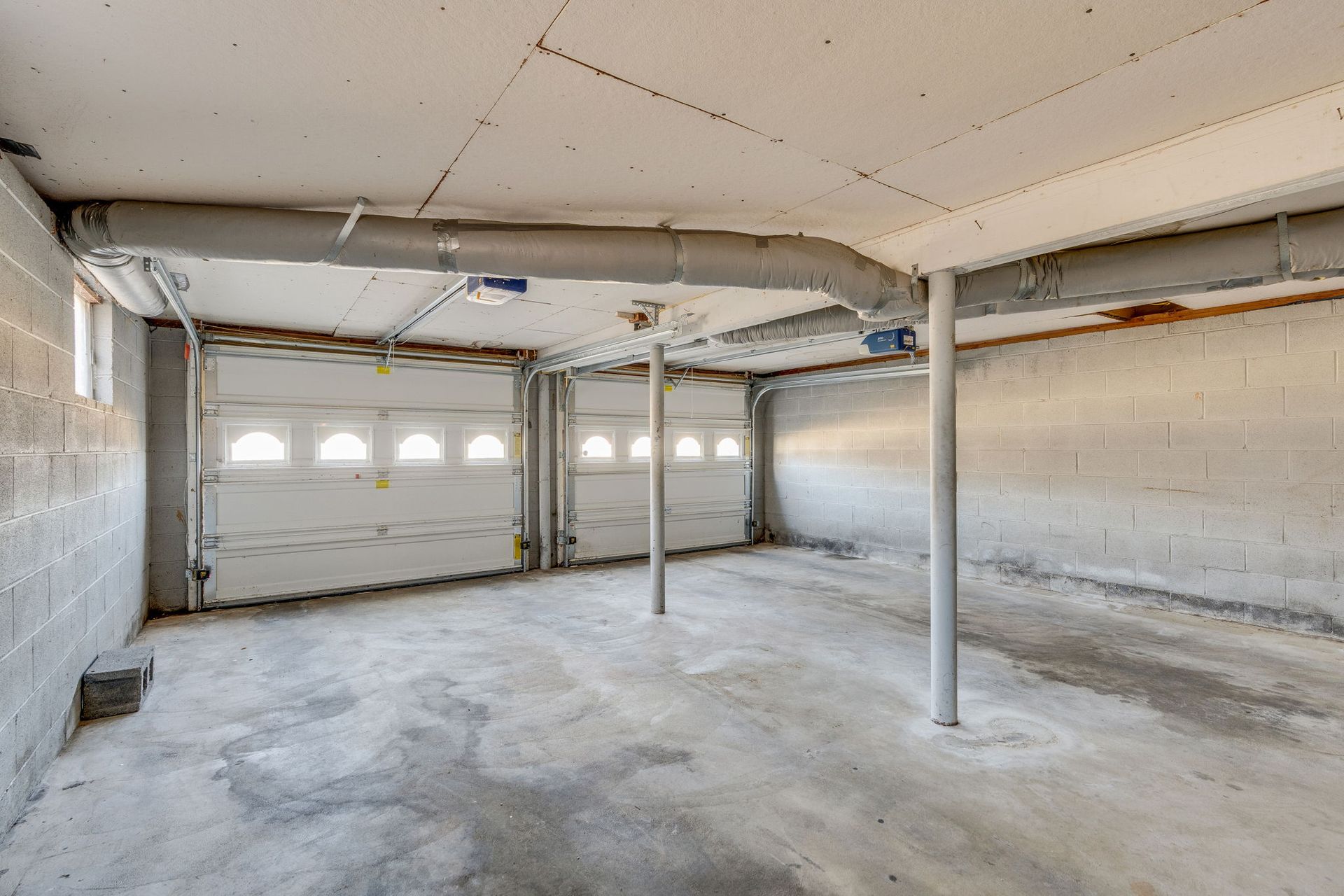 Empty, unfinished garage interior with concrete floor, block walls, garage doors, and support beams.