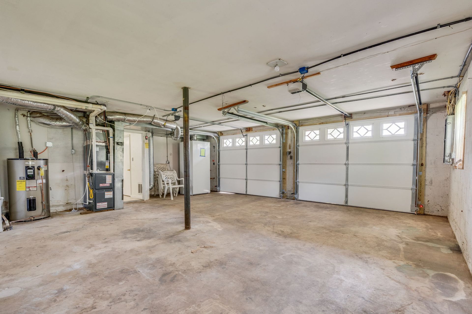 An unfinished garage with a concrete floor, two white paneled garage doors, a water heater, and mechanical equipment.