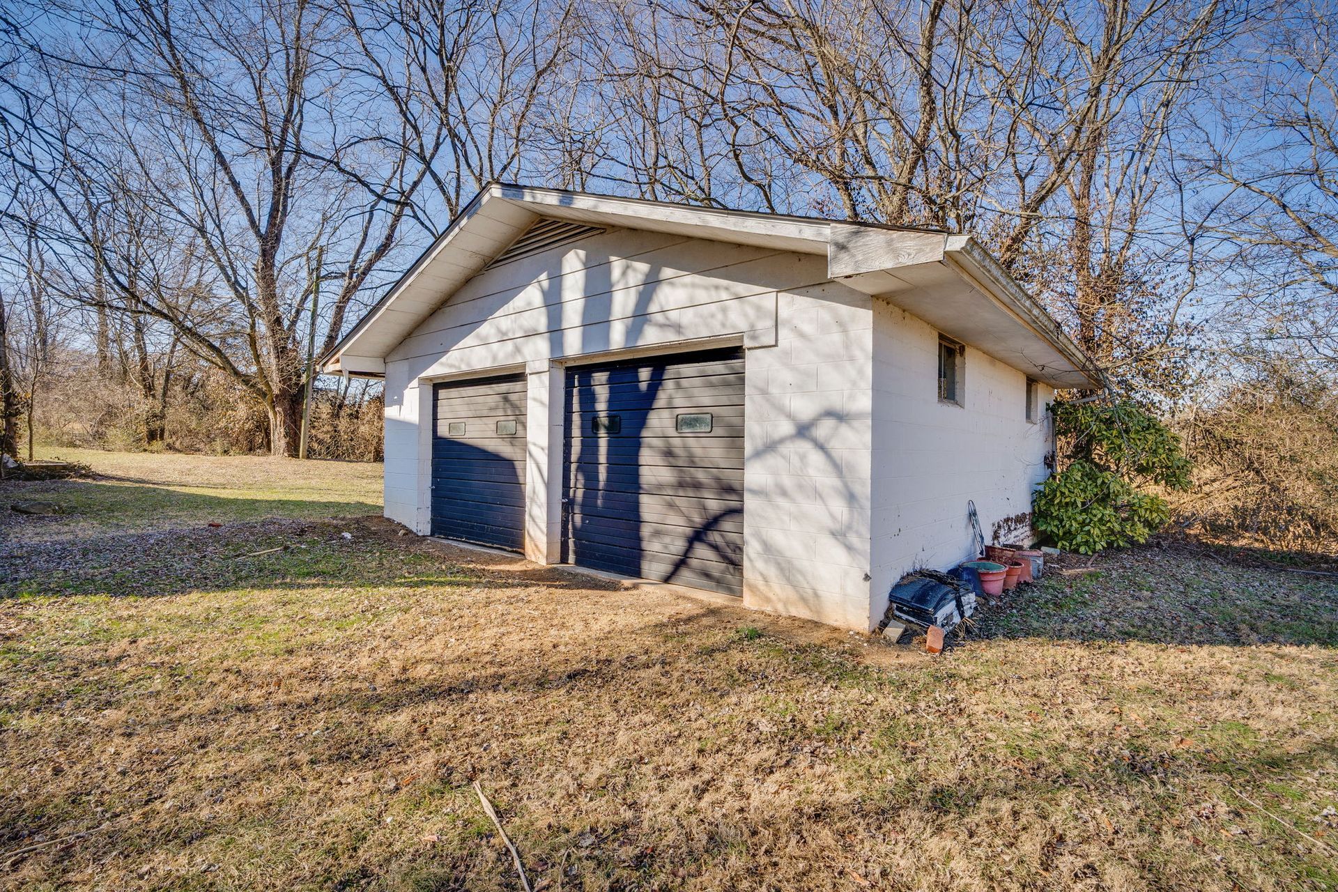 White two-car garage with black doors, surrounded by dry grass and trees under a clear blue sky.
