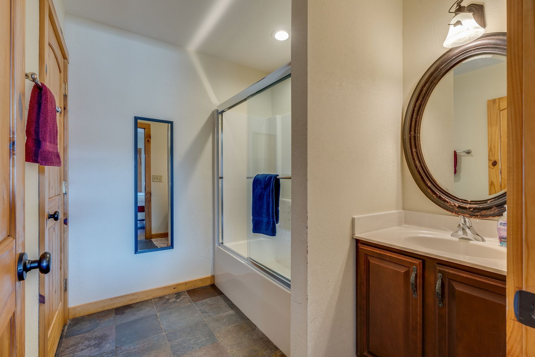 Bathroom with a glass shower, dark wood vanity, and large round mirror.