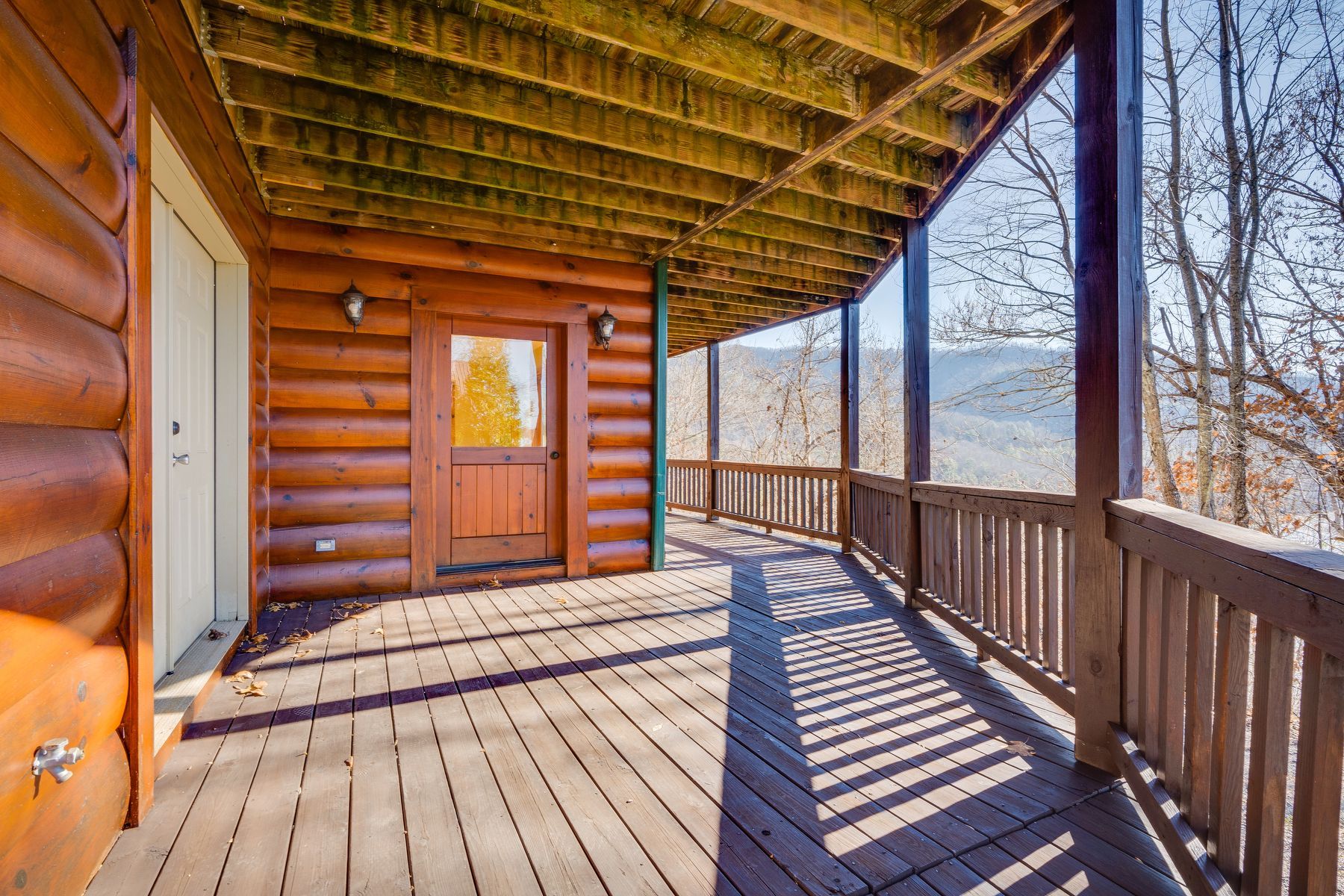 Wooden porch of a log cabin, overlooking a mountain view.