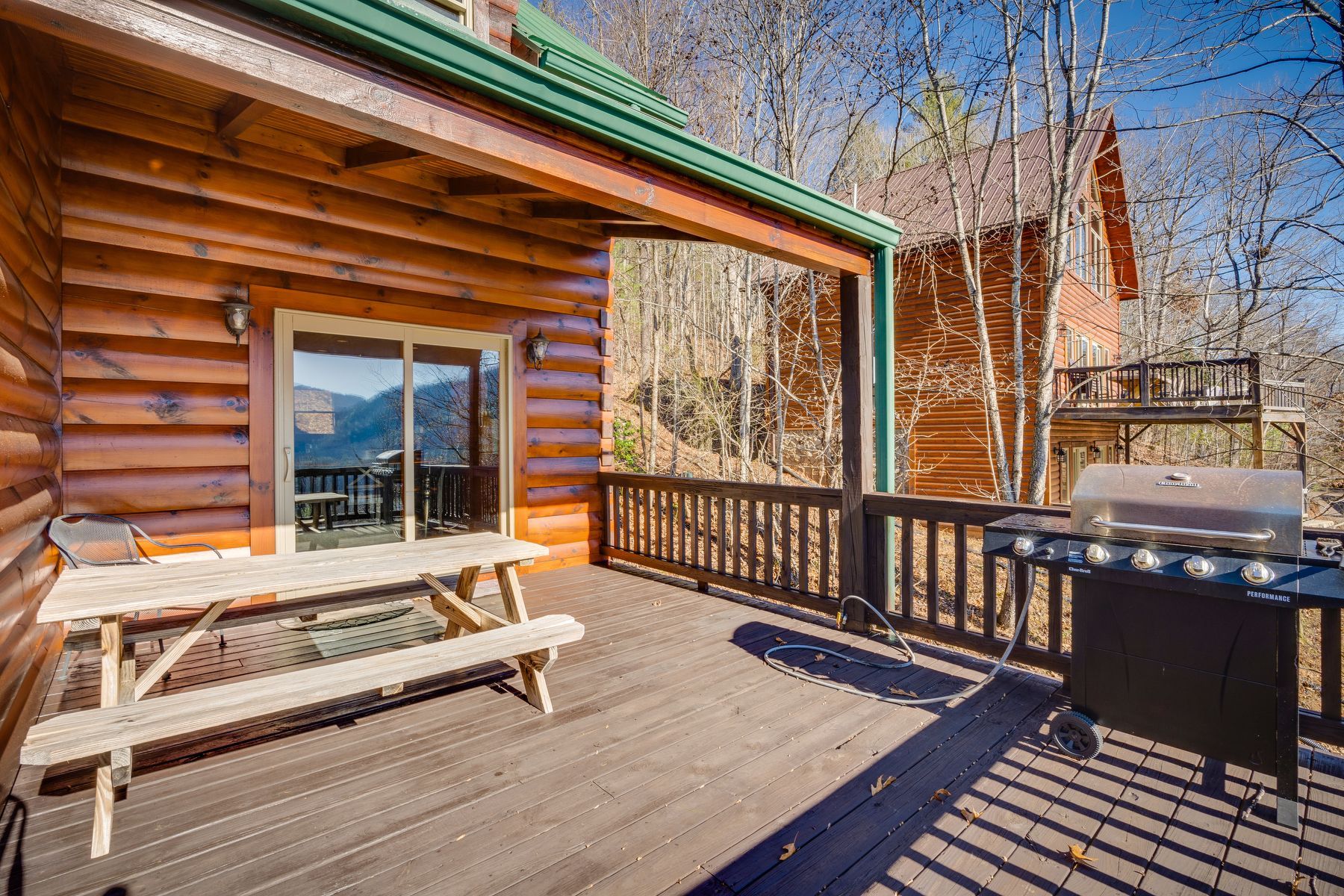 Wooden cabin deck with a picnic table, grill, and mountain view.