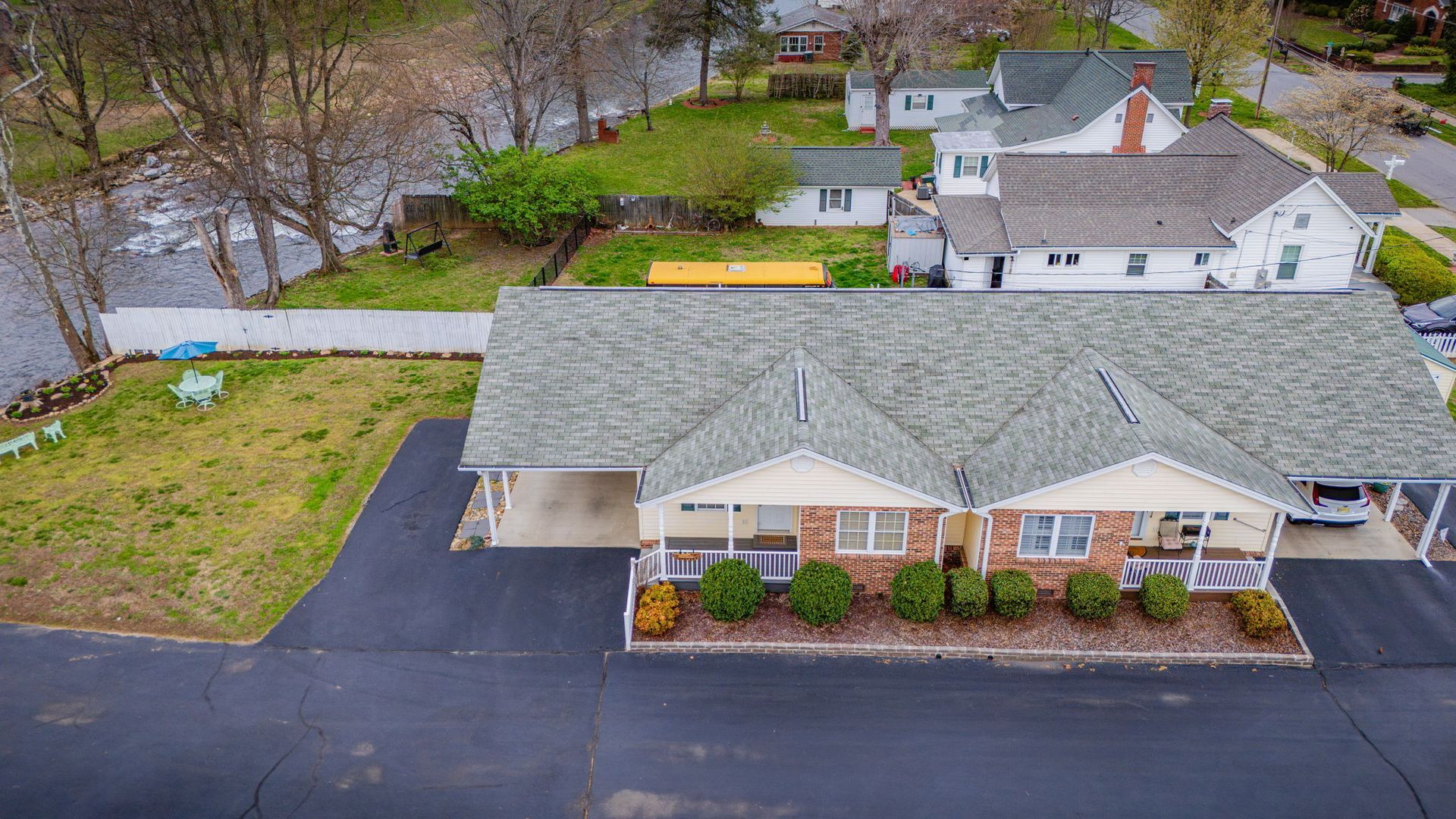 An aerial view of a light-colored, multi-unit building with a grey roof, attached carports, and a black asphalt driveway.