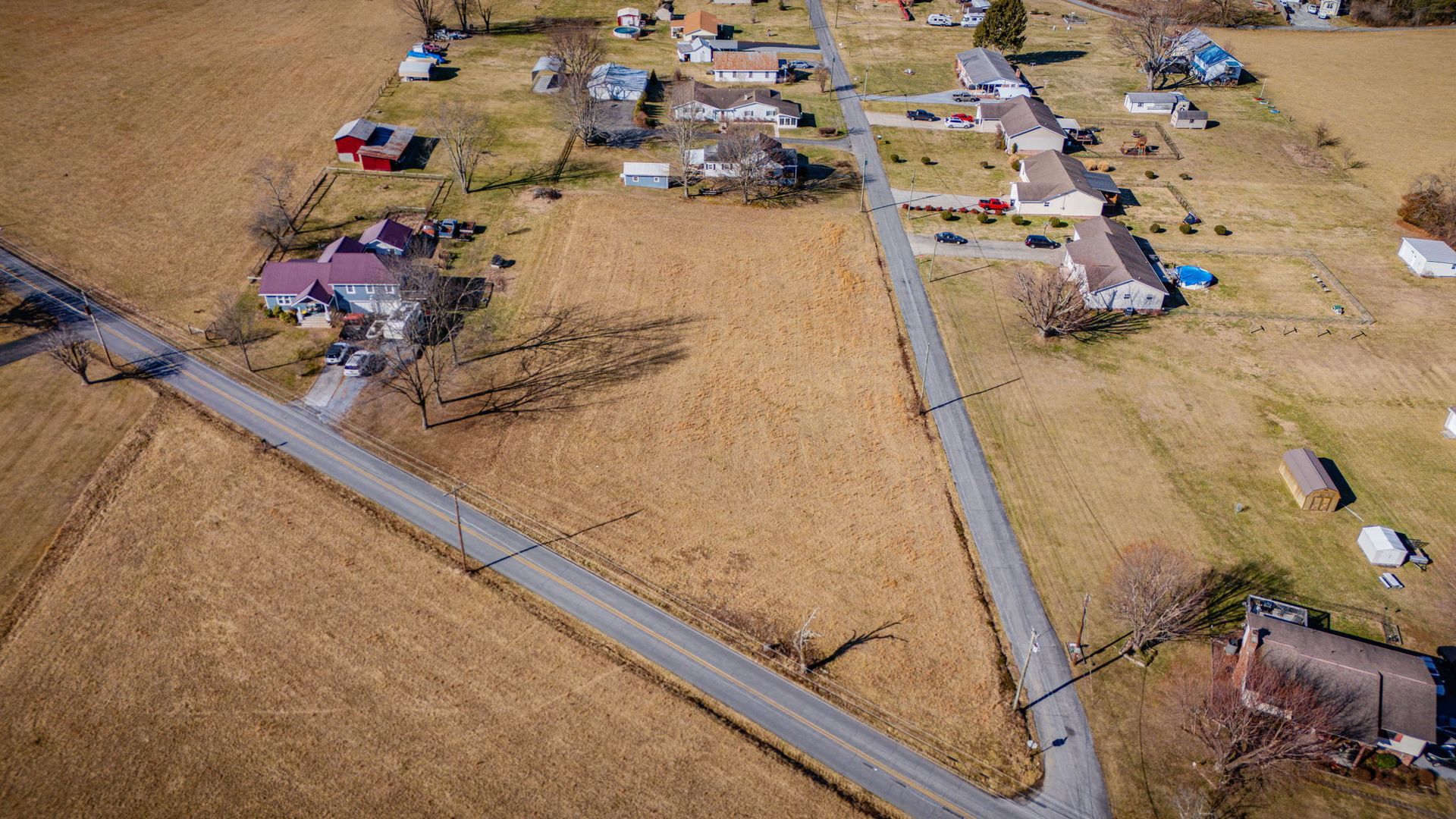 Aerial view of a rural neighborhood with roads, houses, and brown fields.
