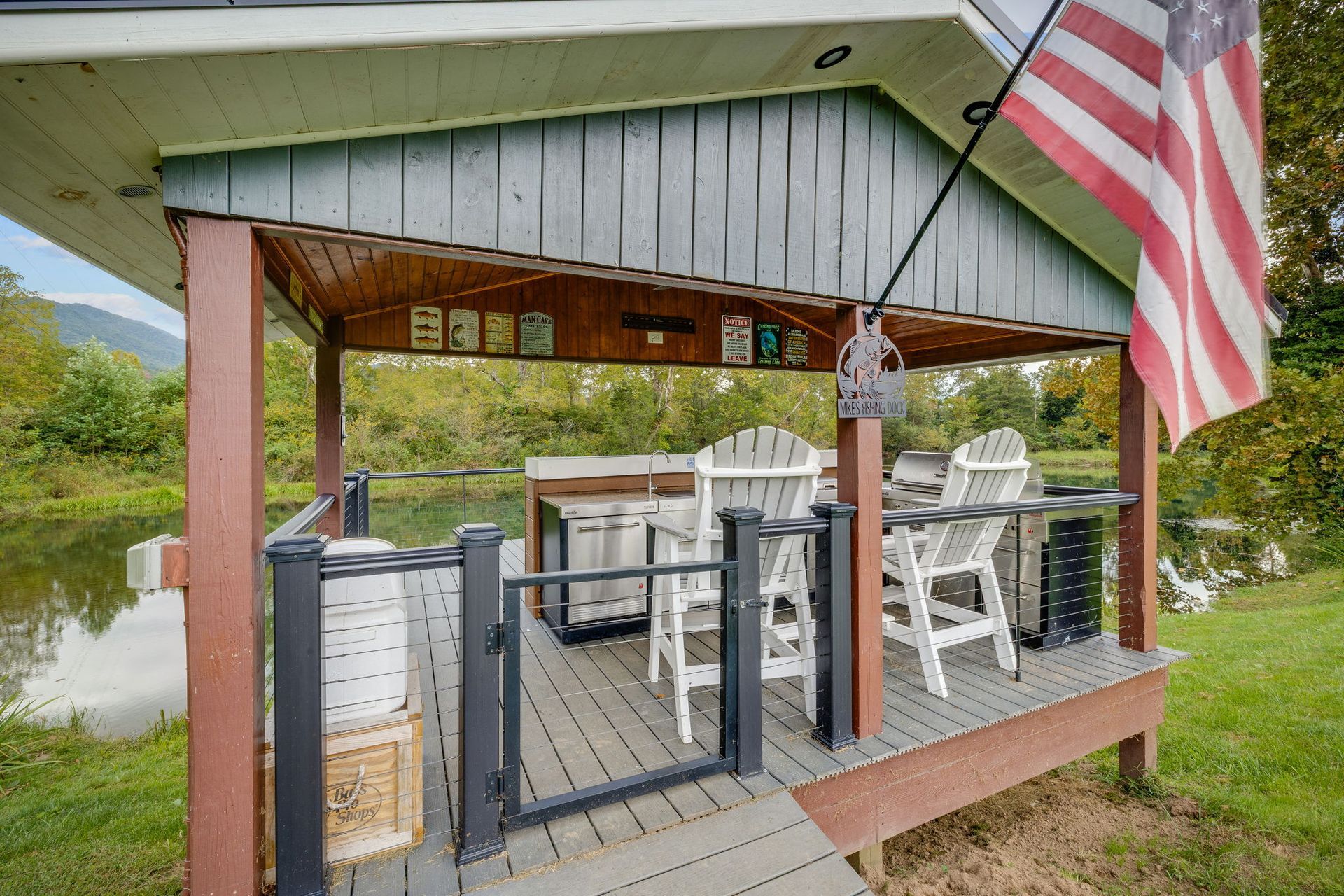 Outdoor deck with seating, grill, and American flag, overlooking water.