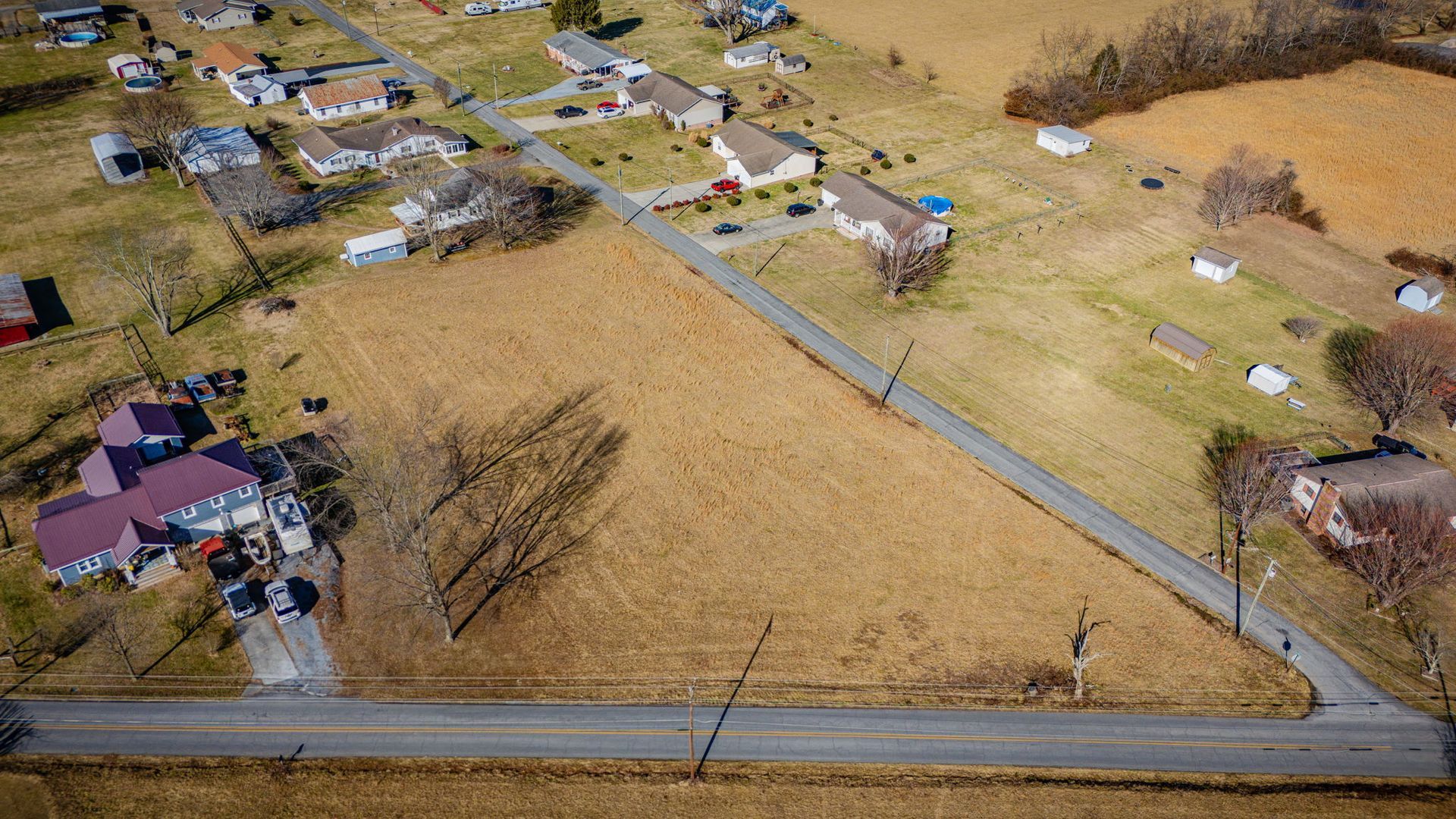 Aerial view of a rural residential area with a road running through a large brown field and houses.
