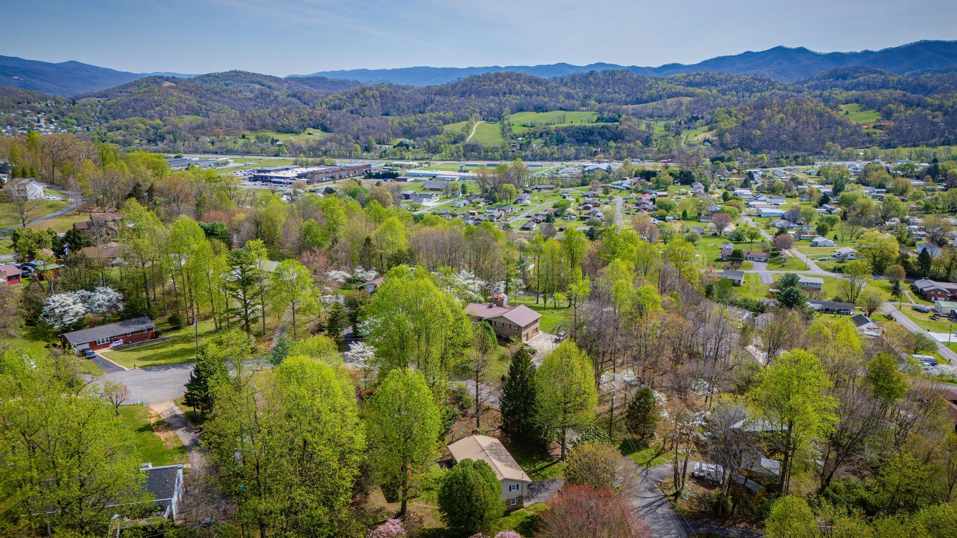 Aerial view of a residential neighborhood nestled among lush trees and hills under a clear blue sky.