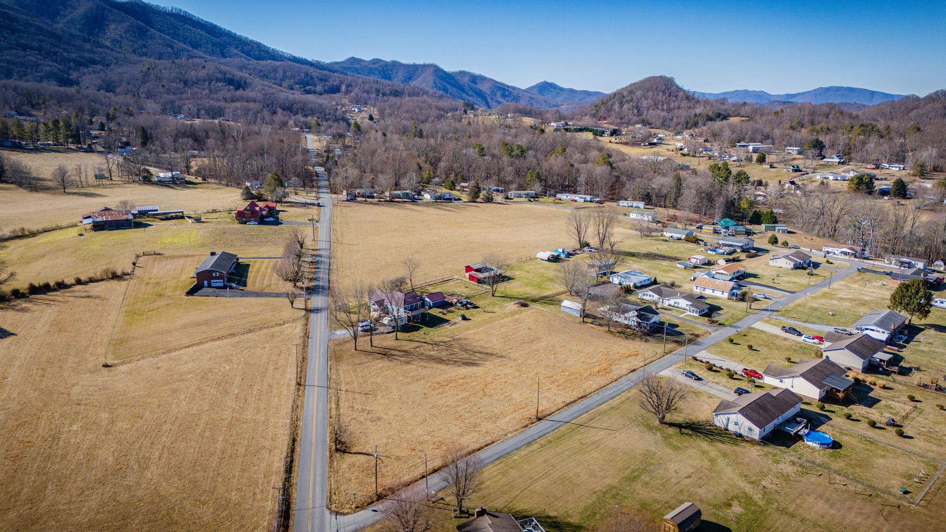 Aerial view of a rural community with houses, fields, and a road against a backdrop of mountains.