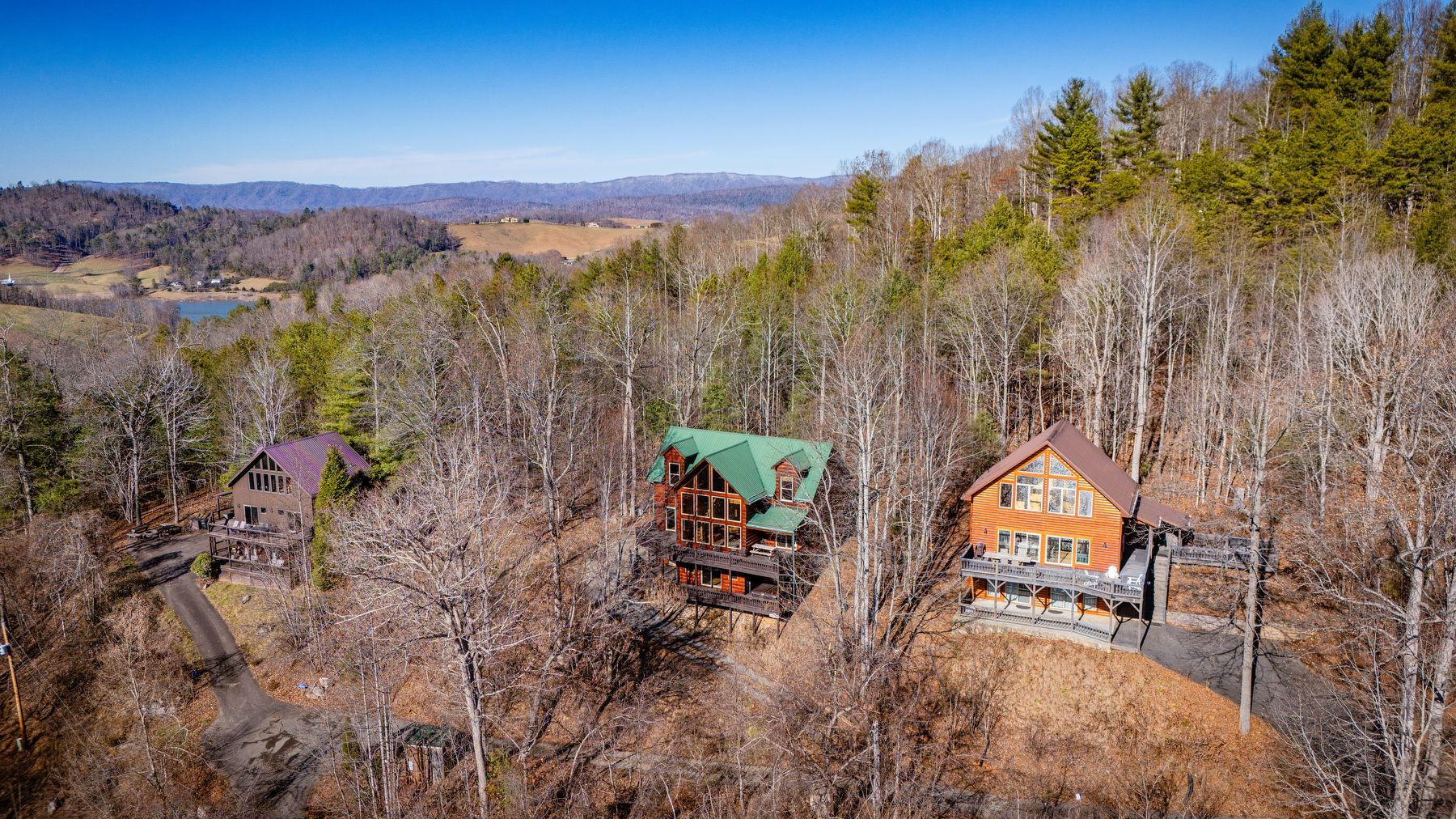 Three cabins nestled in a brown forest on a hillside. Green, orange, and brown cabins under a blue sky.