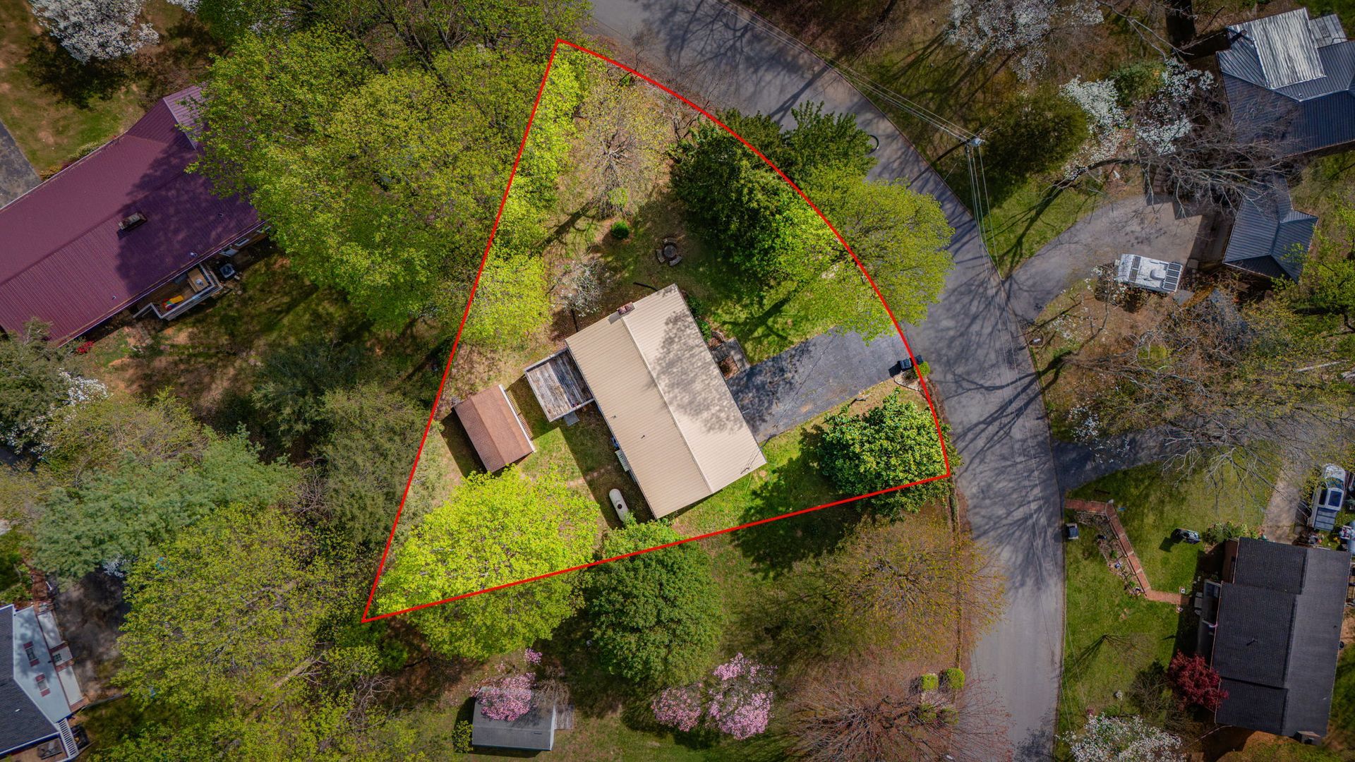 Aerial view of a residential property outlined in red, featuring a house, a shed, and trees on a corner lot.