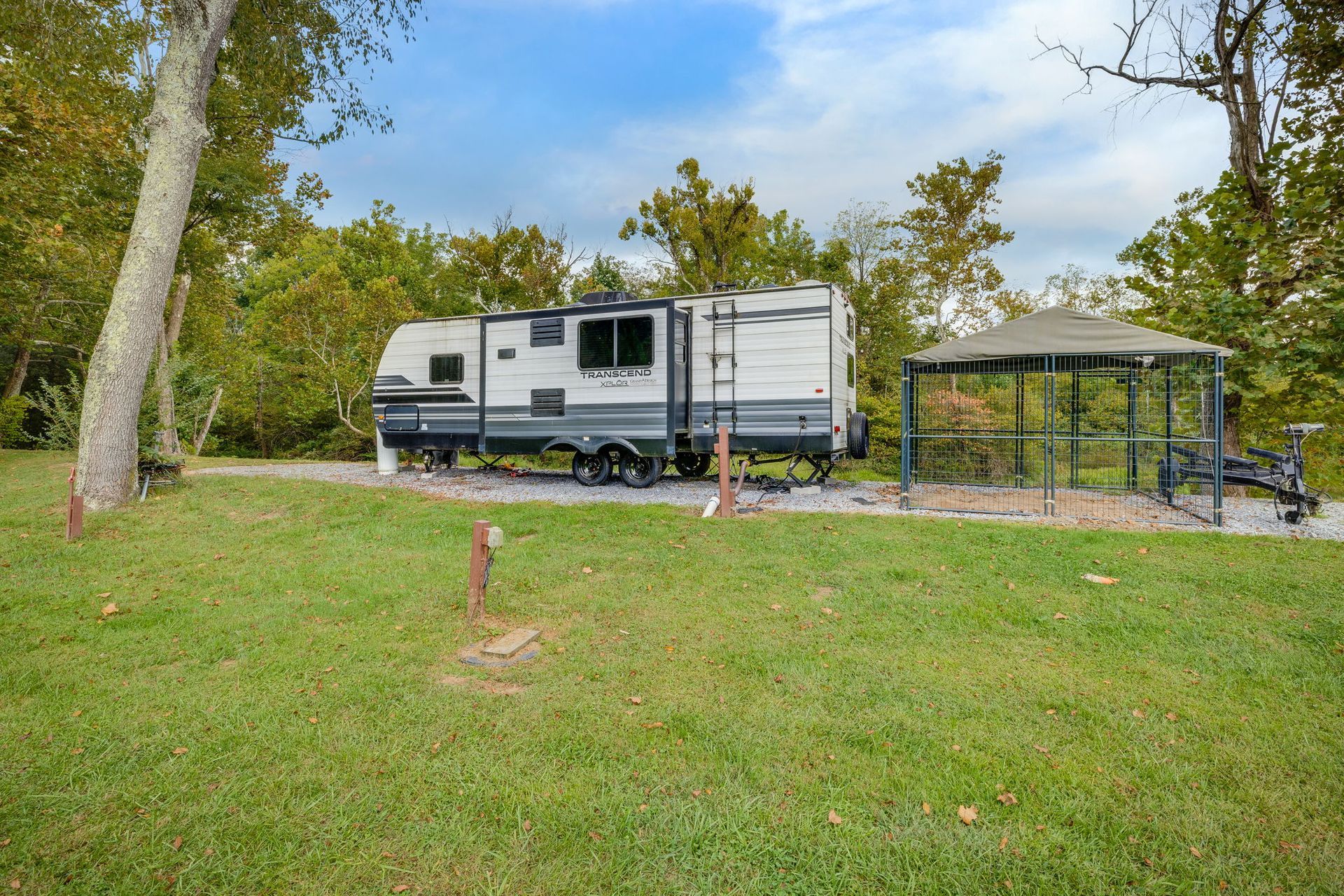RV parked at a campsite next to a gazebo in a grassy area, trees in the background.