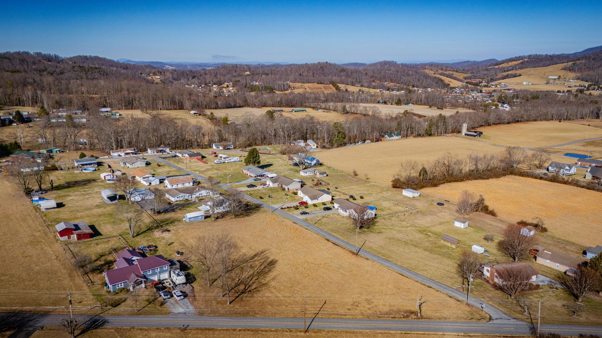 Aerial view of a rural community with houses, roads, and fields, under a blue sky.