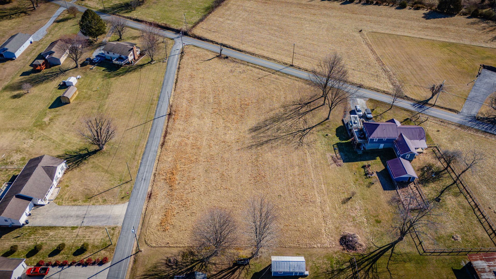 Aerial view of a mostly empty field bordered by roads and houses in a rural area.