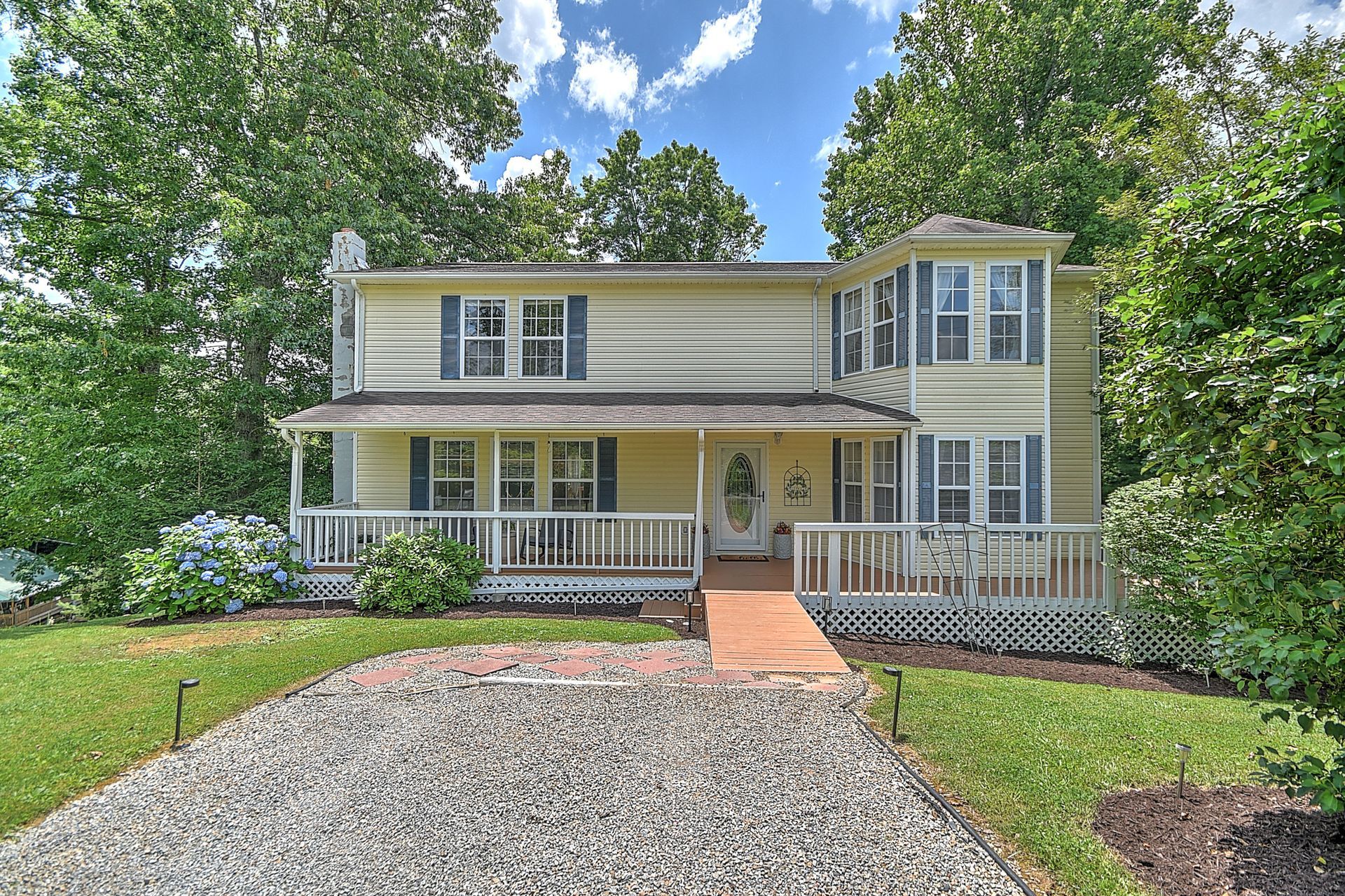 A large yellow house with a large porch and a gravel driveway.