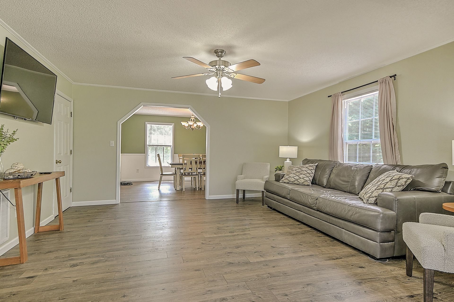 A living room with a couch , chairs , a television and a ceiling fan.