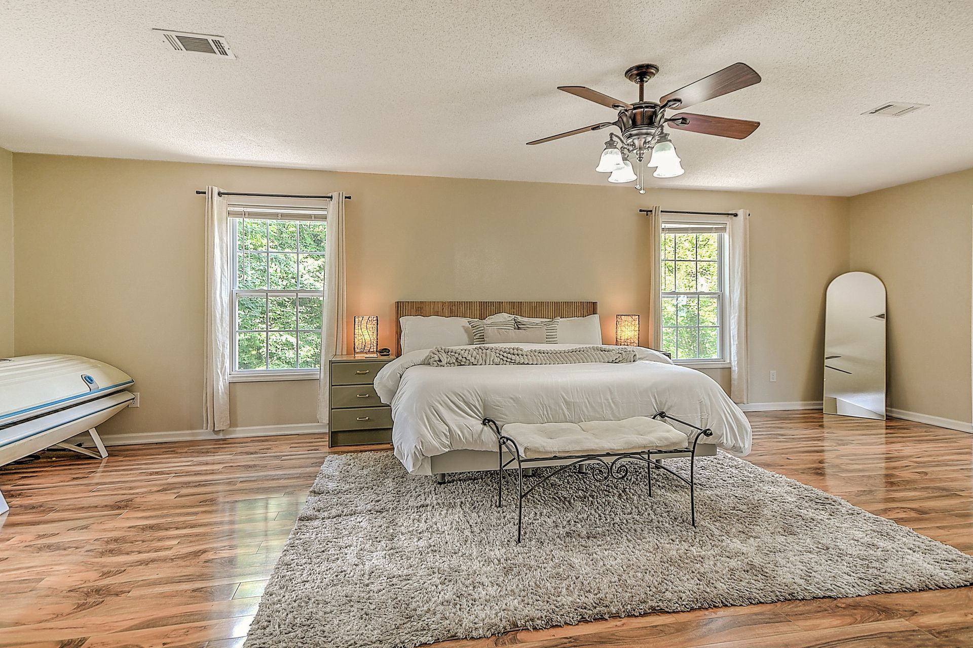 A large bedroom with a king size bed , a rug , a bench and a ceiling fan.