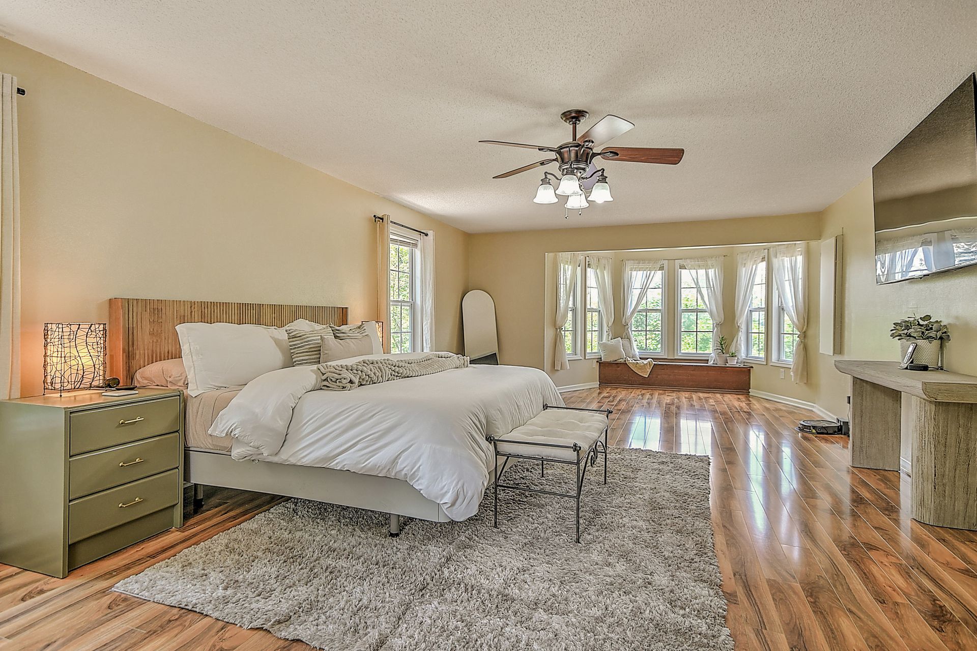 A bedroom with a bed , dresser , nightstand , rug and ceiling fan.