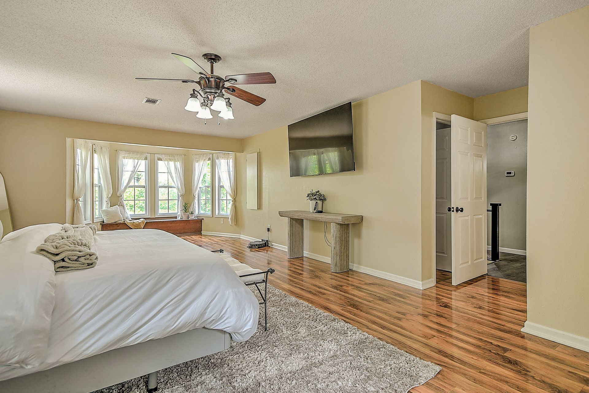 A large bedroom with a king size bed , hardwood floors , a ceiling fan and a flat screen tv.