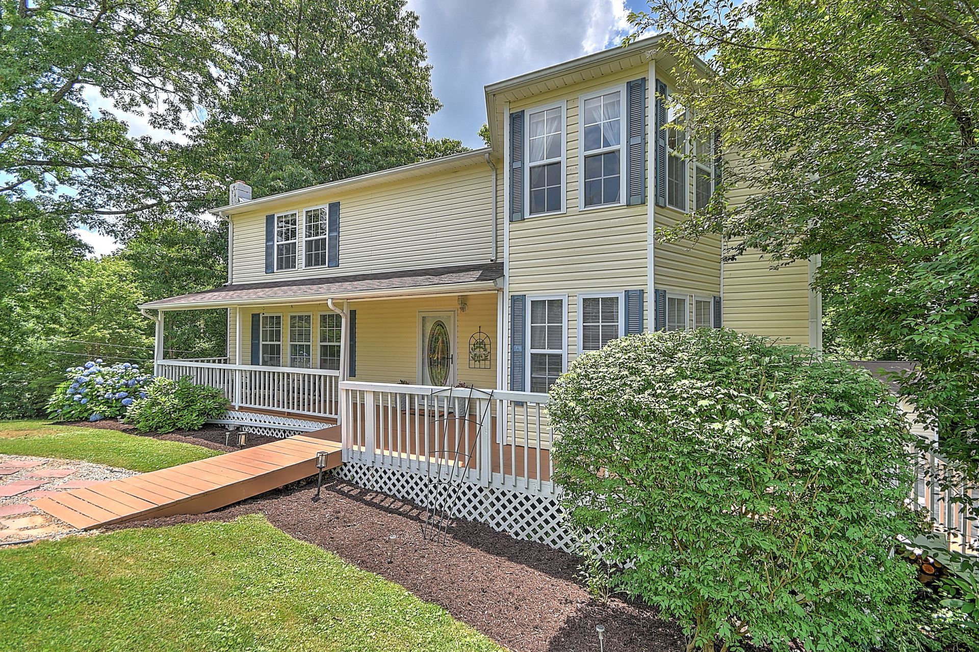 A large yellow house with a large porch and a ramp leading to it.