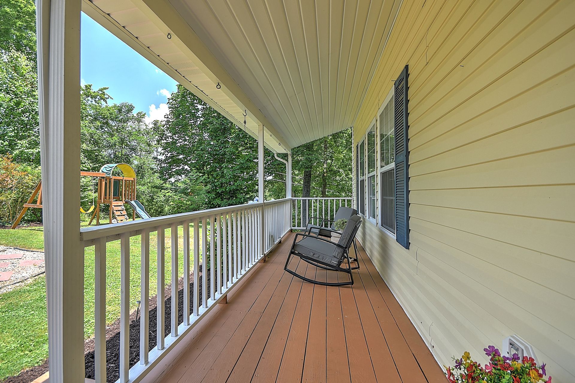 A porch with rocking chairs and a playground in the background