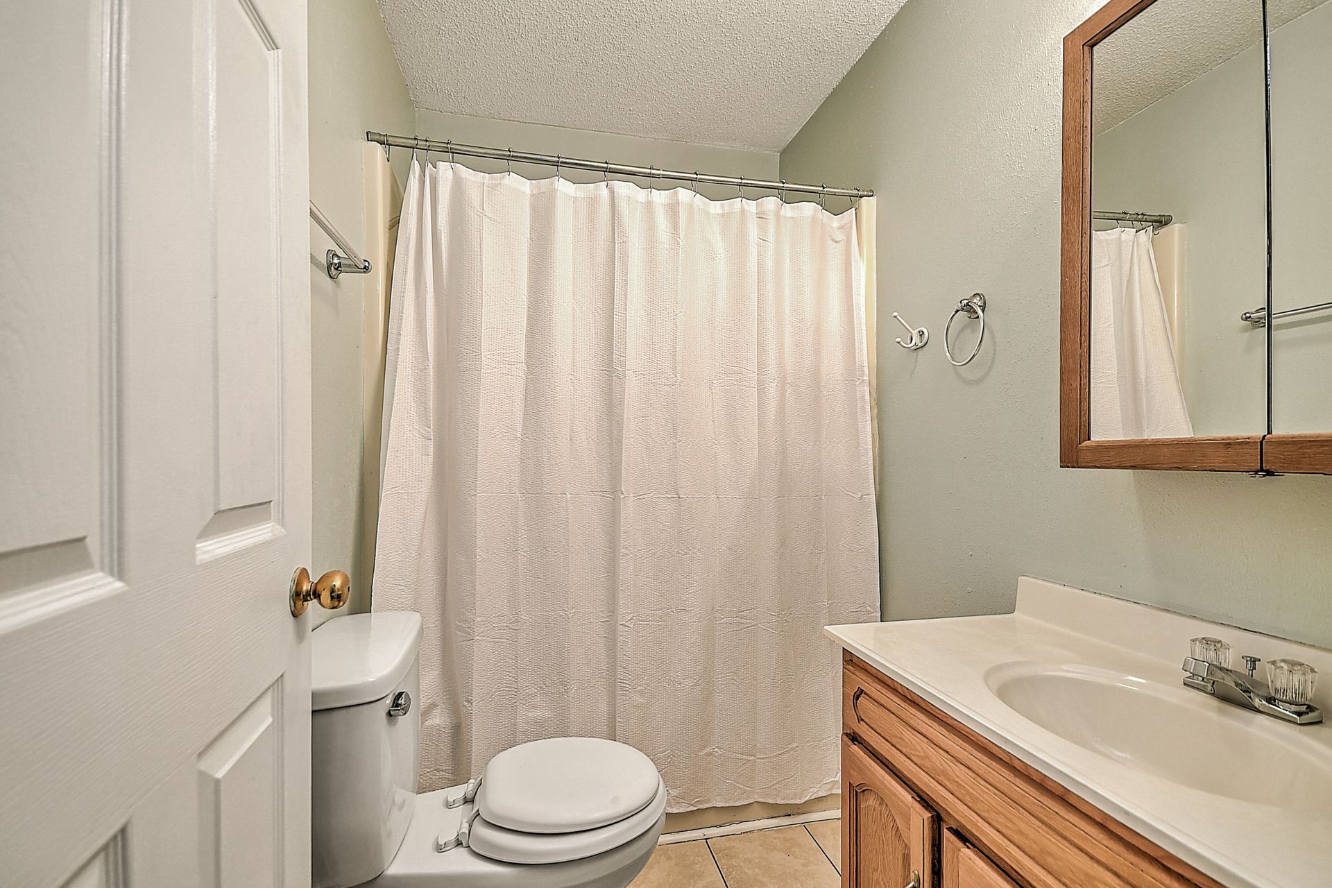 A bathroom with a toilet , sink , mirror and shower curtain.