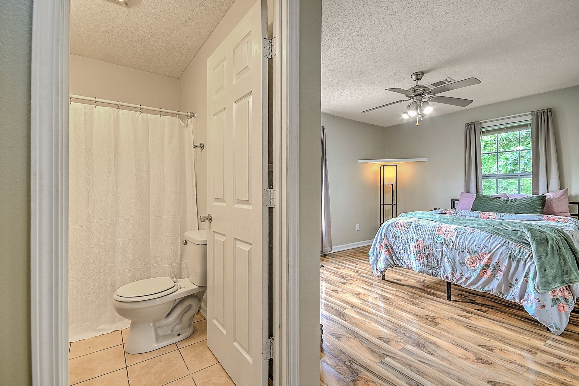 A bedroom with a bed , toilet , shower and ceiling fan.