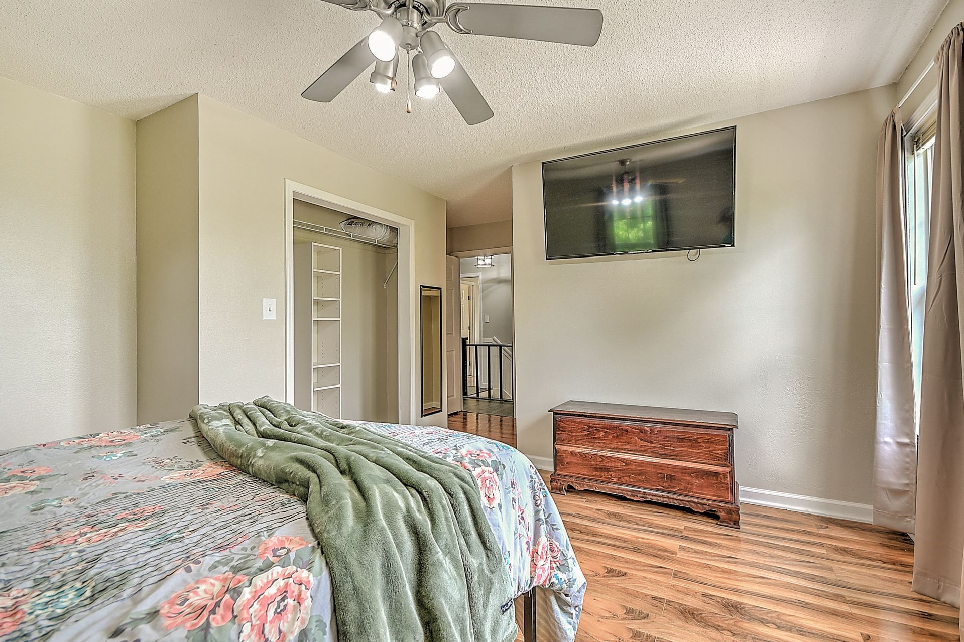 A bedroom with a bed , dresser , television and ceiling fan.