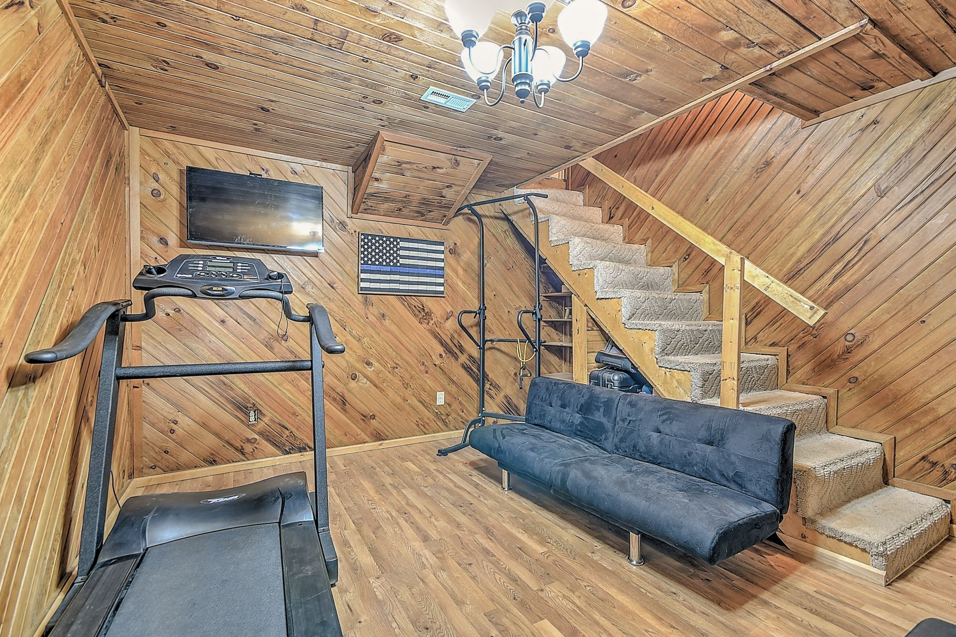 A living room with a couch , treadmill , television and stairs.