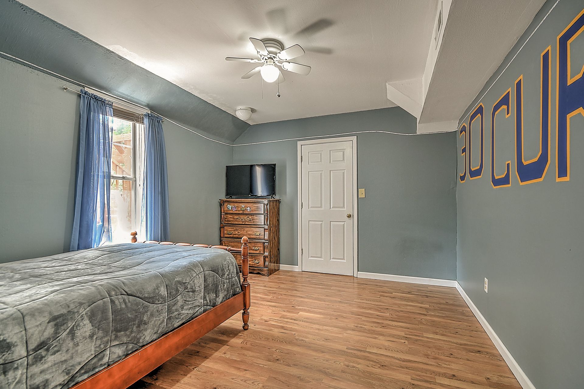 A bedroom with a bed , dresser , television and a ceiling fan.
