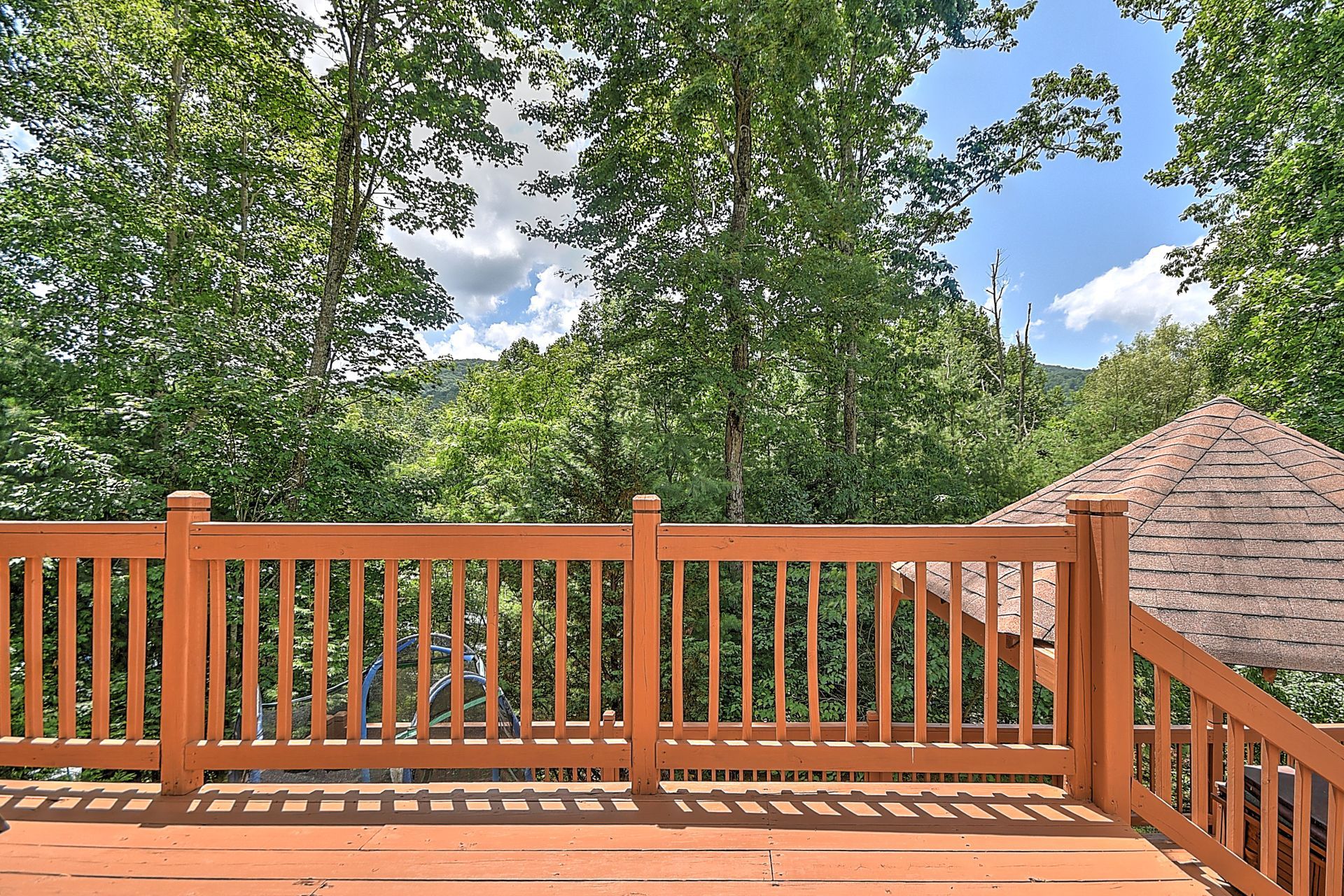 An empty deck with a wooden railing and trees in the background