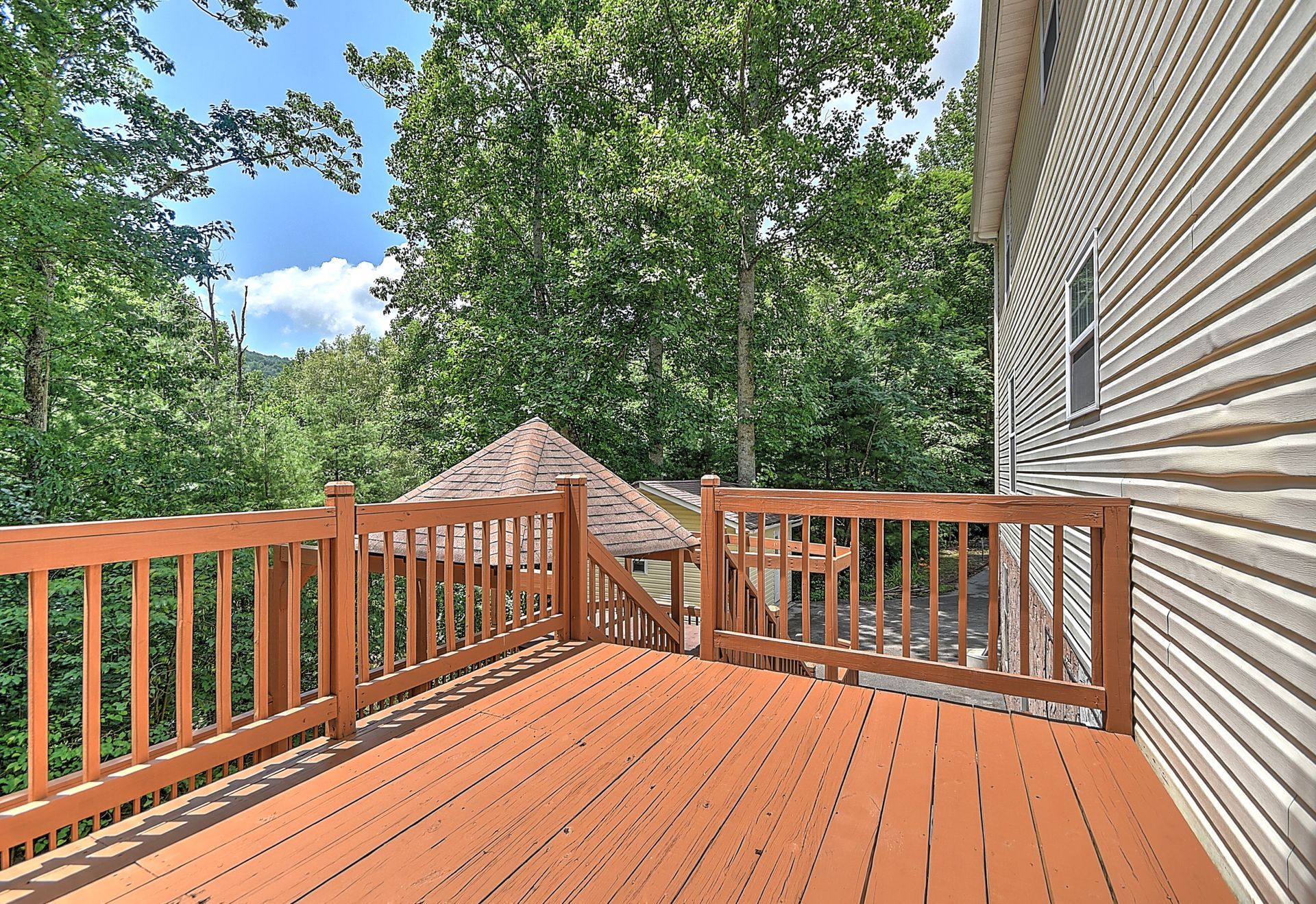 An empty deck with a wooden railing and trees in the background.