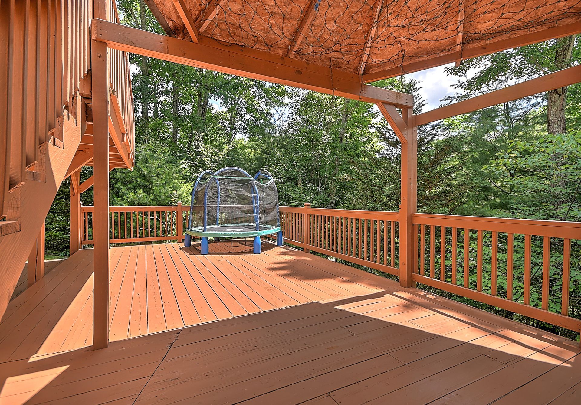 A wooden deck with a bench and trees in the background