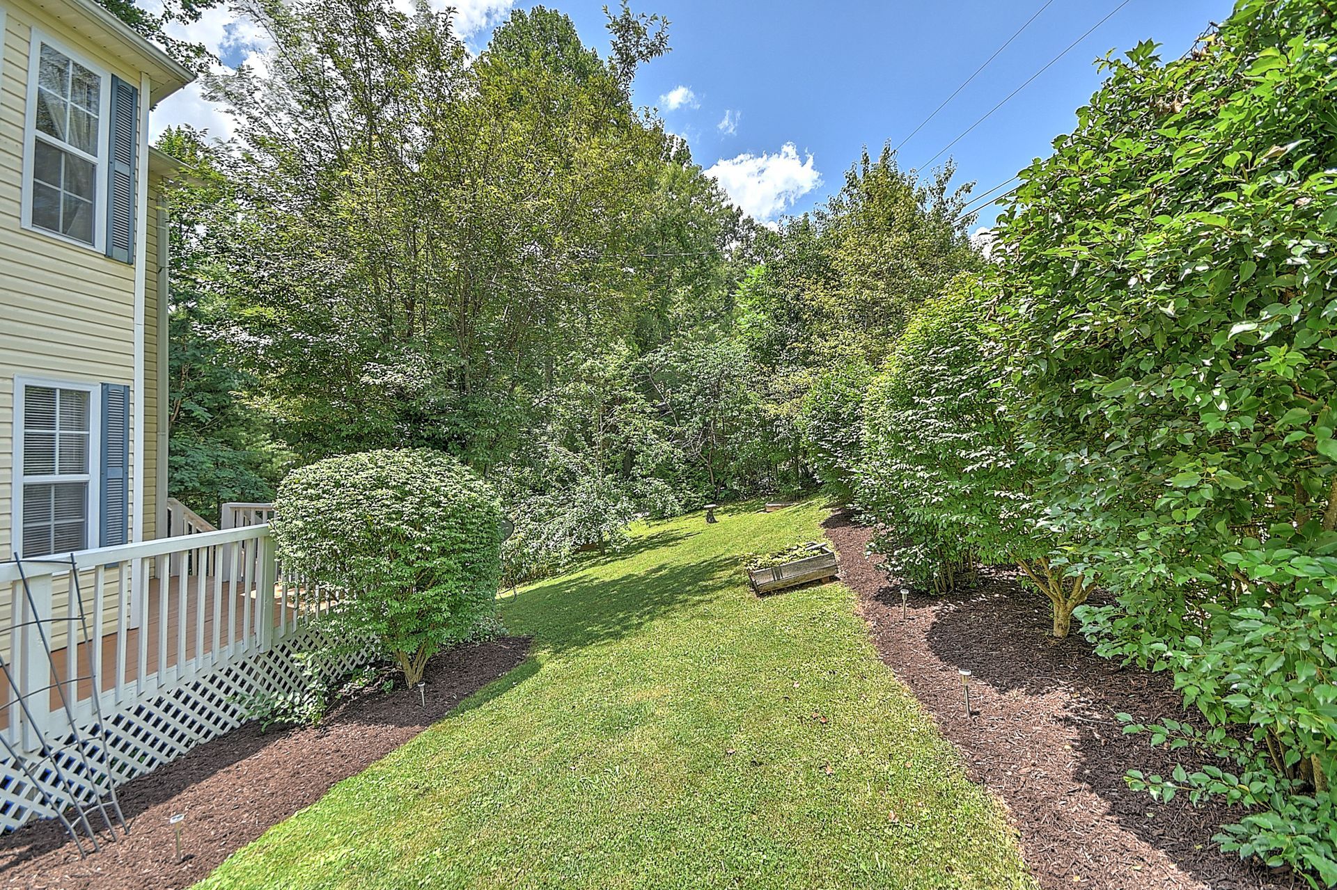There is a large lawn in front of a house surrounded by trees and bushes.