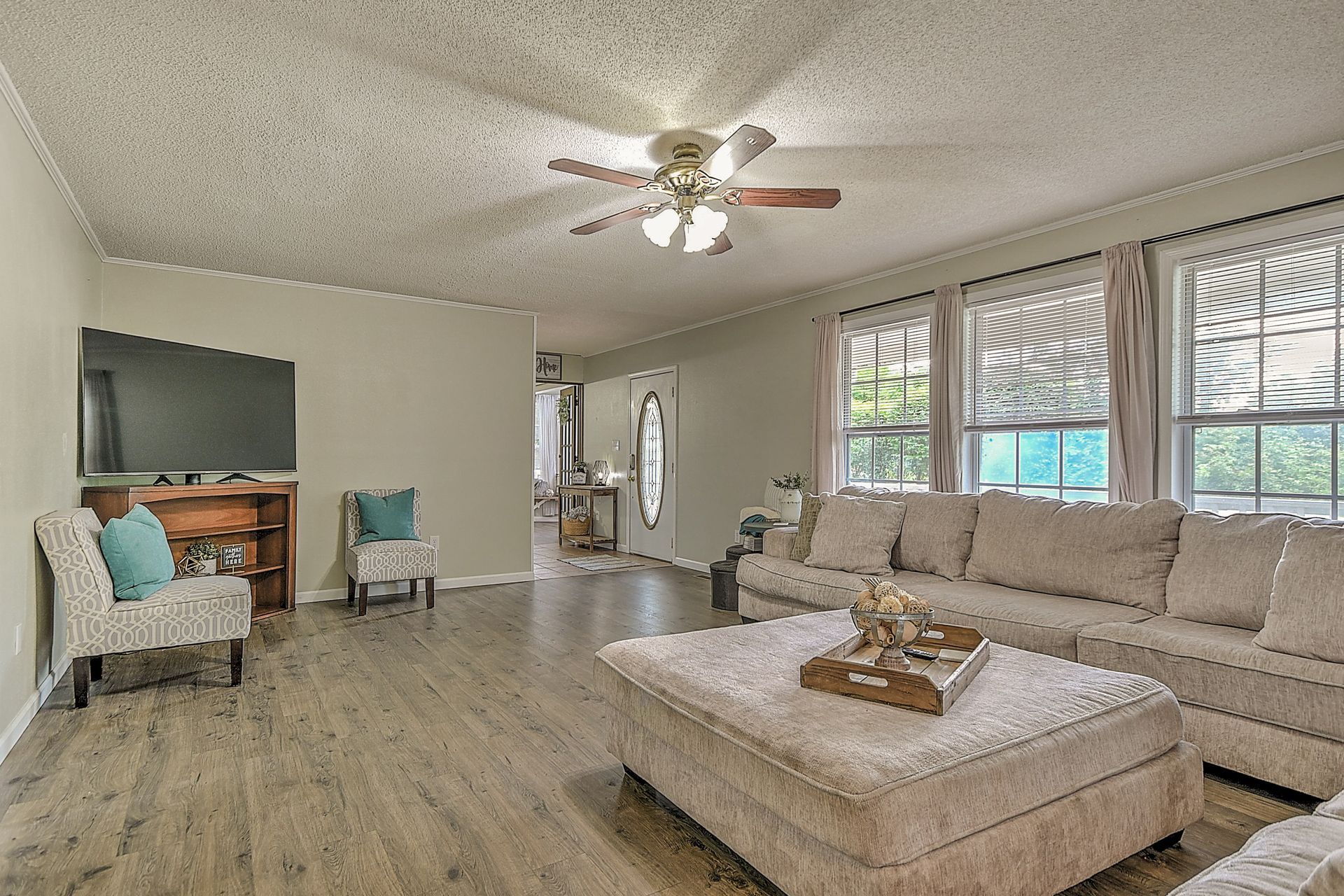 A living room with a couch , chair , coffee table , television and ceiling fan.