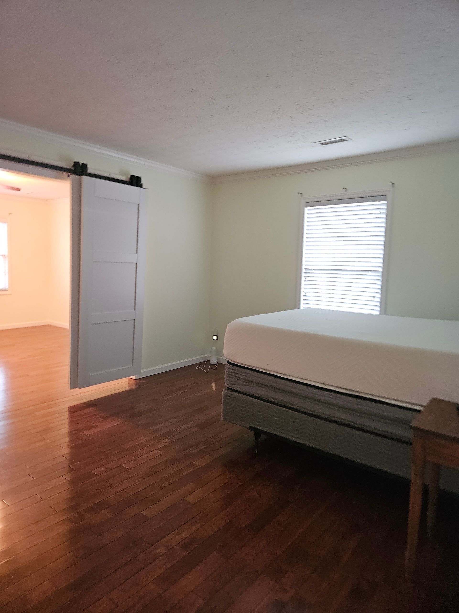 Bedroom with wood floors, a bed with a white mattress, and a white sliding barn door leading to an adjacent room.