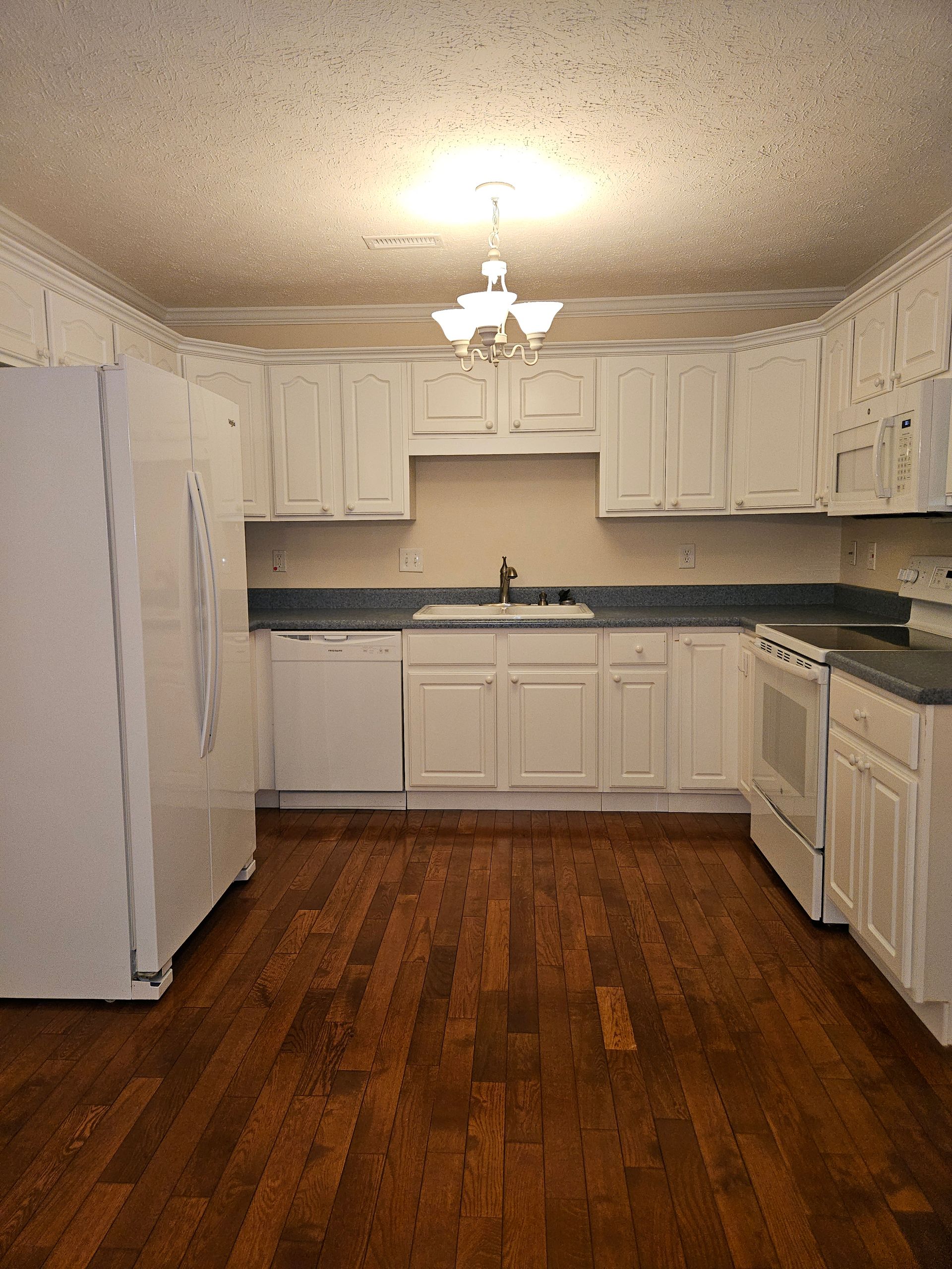 A white kitchen with wooden floors, blue countertops, white cabinets, and white appliances under a ceiling light.
