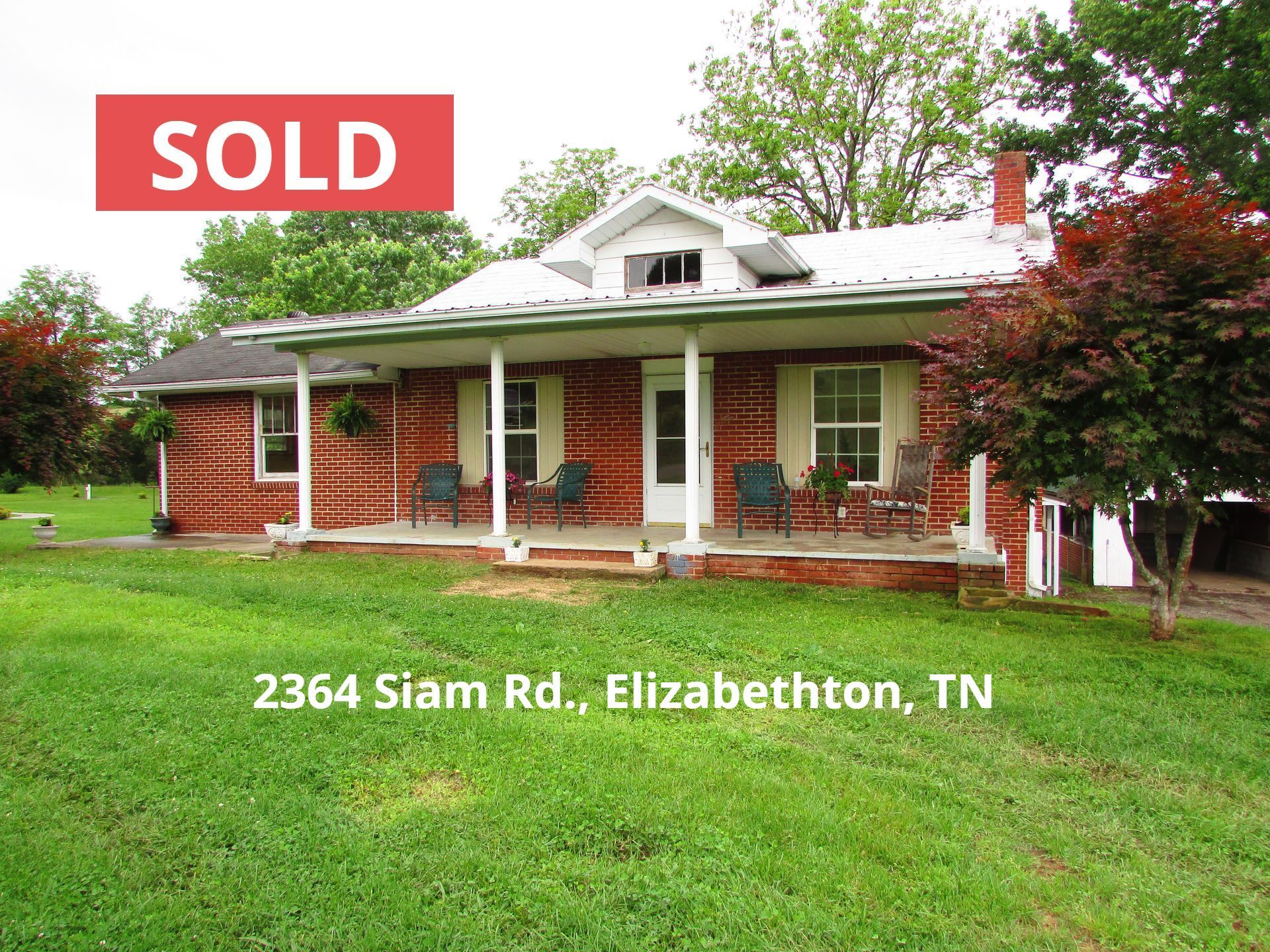 A brick house with a porch and chairs in front of it.