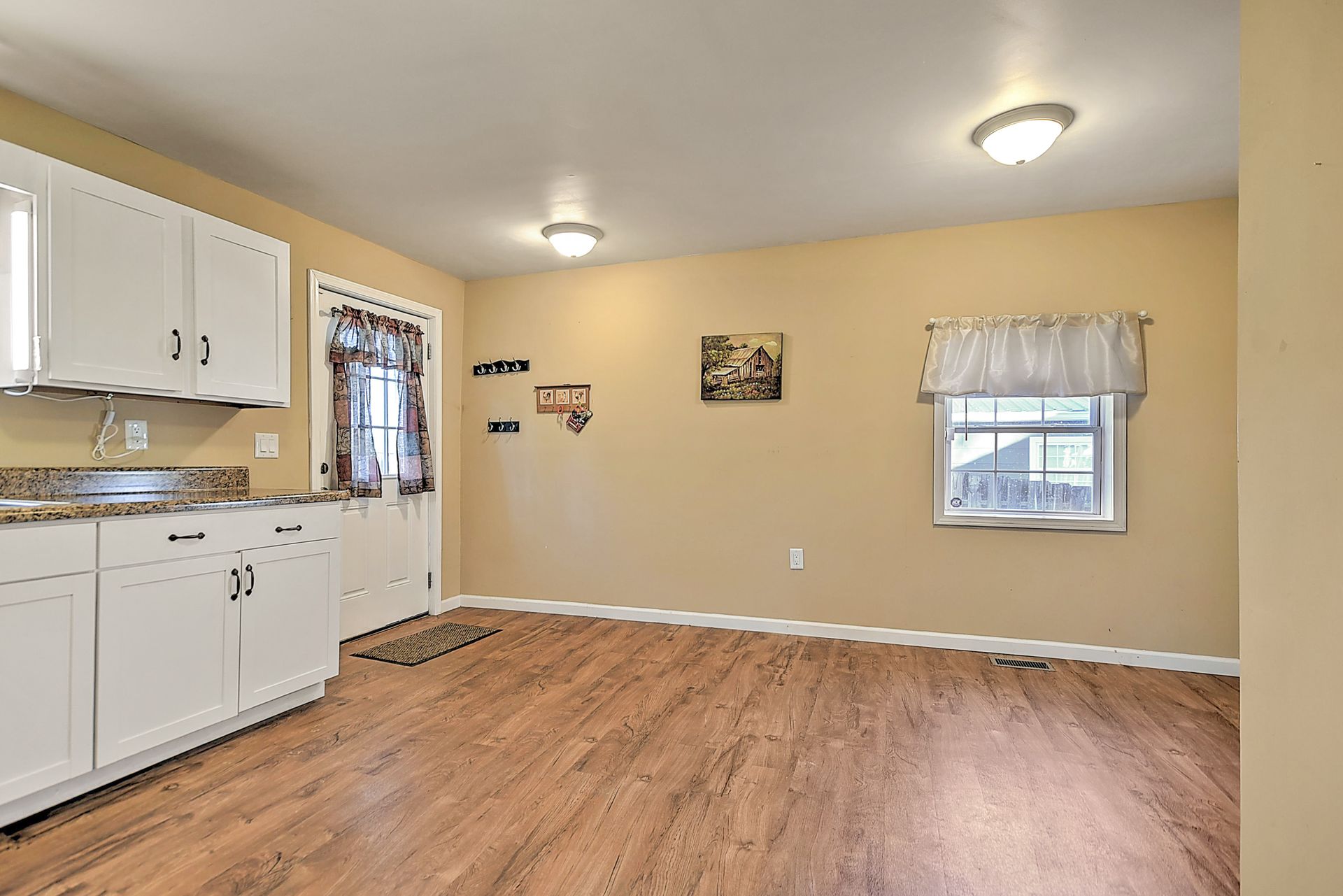 Kitchen with white cabinets, wood flooring, and tan walls; a doorway leads outside.
