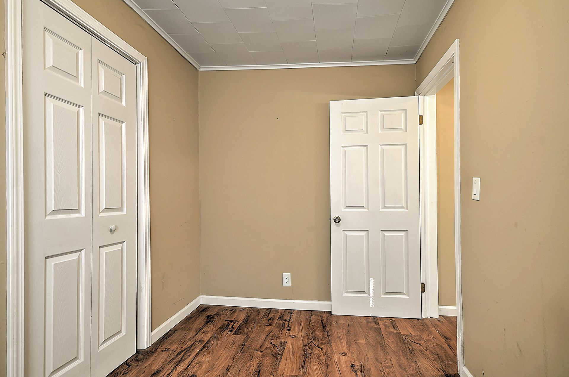 Empty room with closed white doors and tan walls, hardwood floor, and a white ceiling.