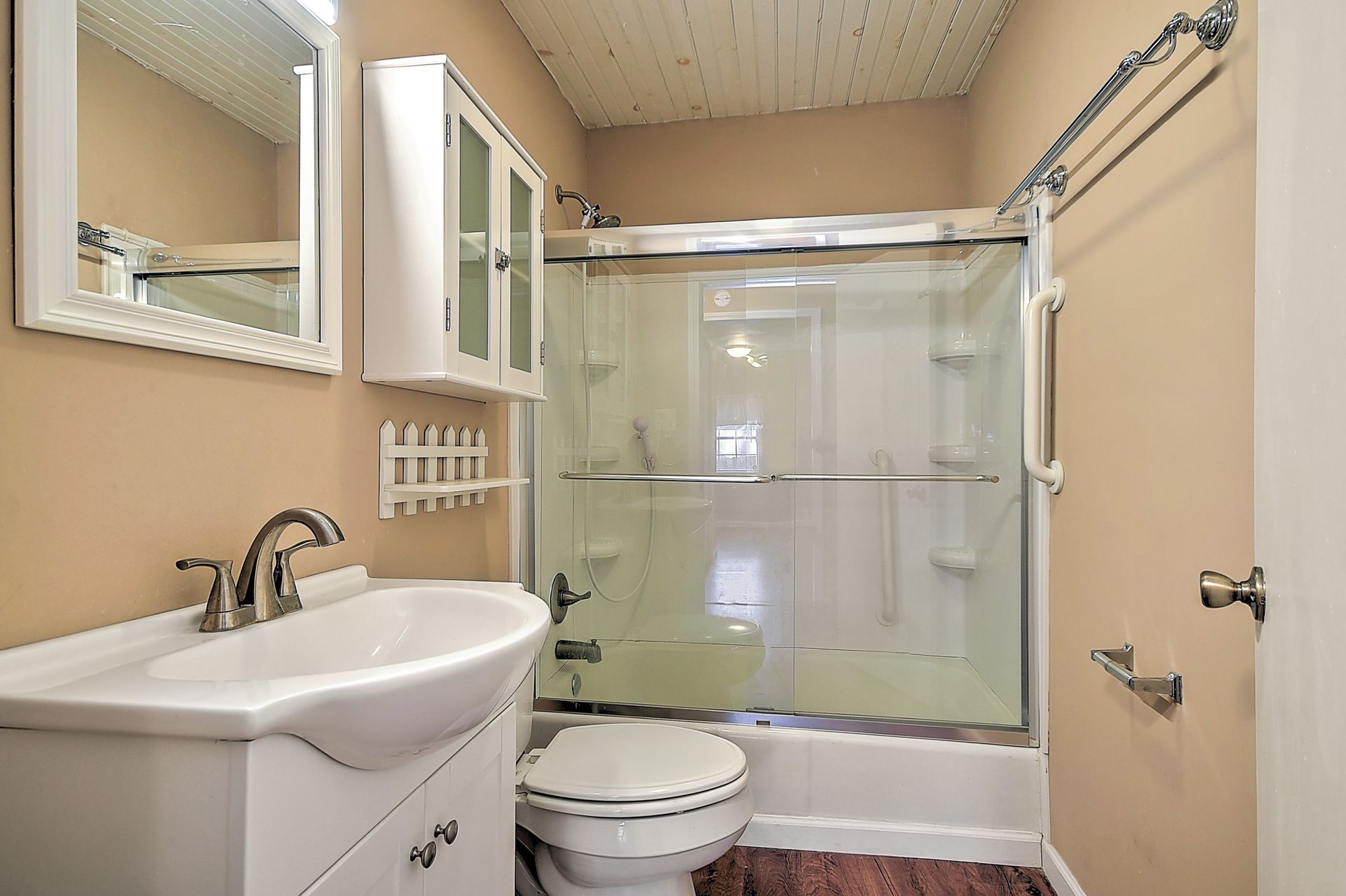 Small bathroom with white sink, toilet, and shower/tub, beige walls, and wooden floor.