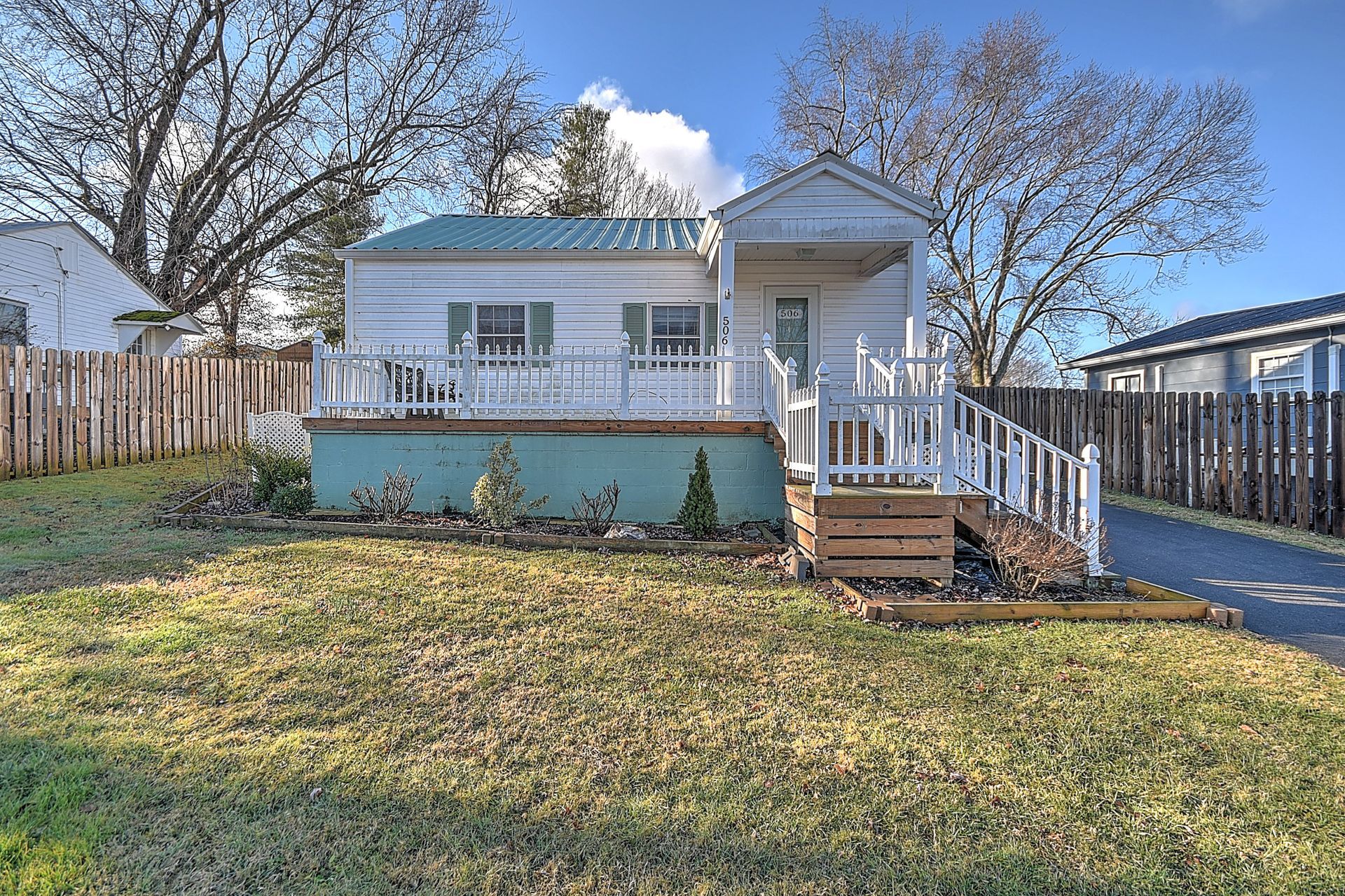 Small white house with porch and yard, blue sky.