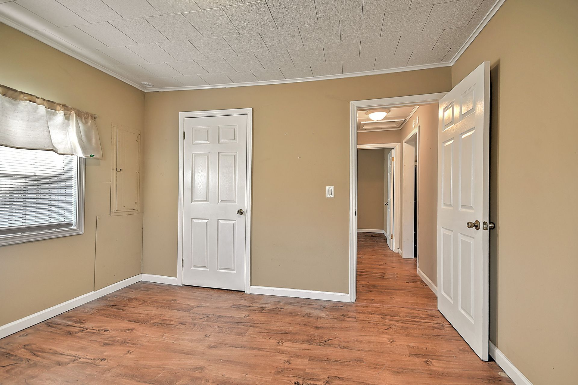 Empty room with beige walls, white doors, and a hallway visible.