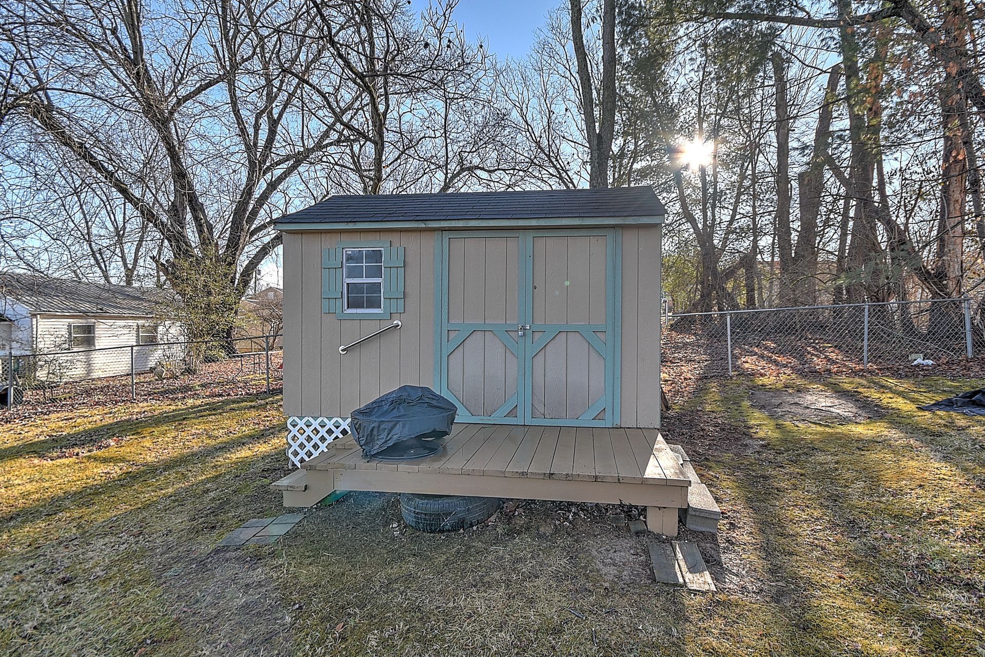 A small wooden shed with a window and double doors sits on a raised platform in a yard.