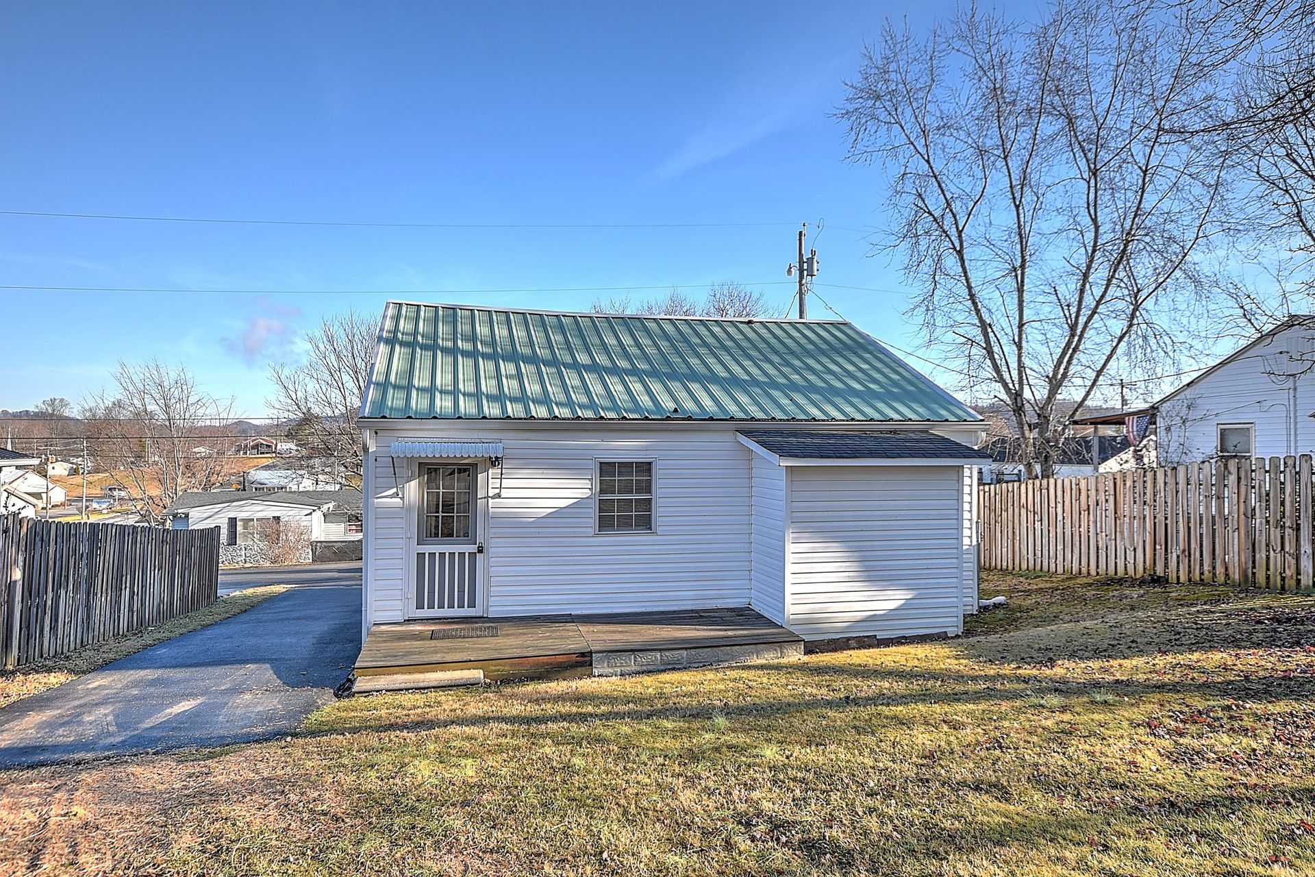 Small white house with green roof, sitting on a grassy lot, sunny day.