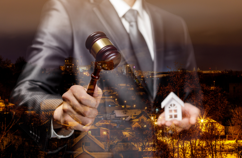 A man in a suit is holding a gavel and a small house WITH A CITY IN THE BACKGROUND