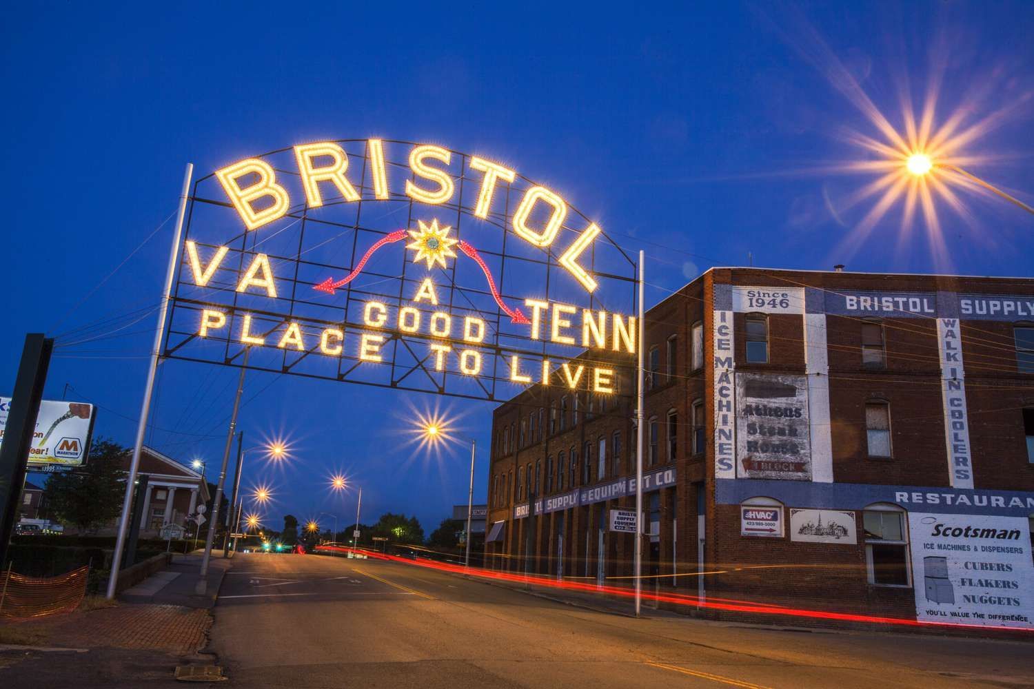 A sign that says Bristol TN/VA a good tenn place to live  lit up at night arching over State Street in Bristol