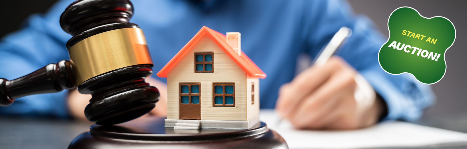 A gavel next to a miniature house with a person signing documents, symbolizing a real estate auction.