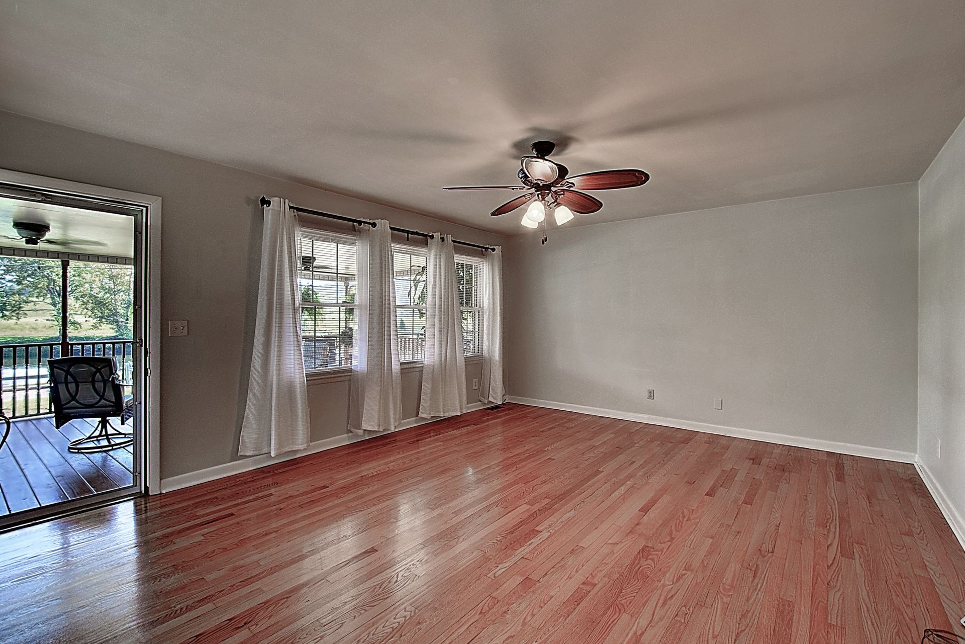 An empty living room with hardwood floors and a ceiling fan.